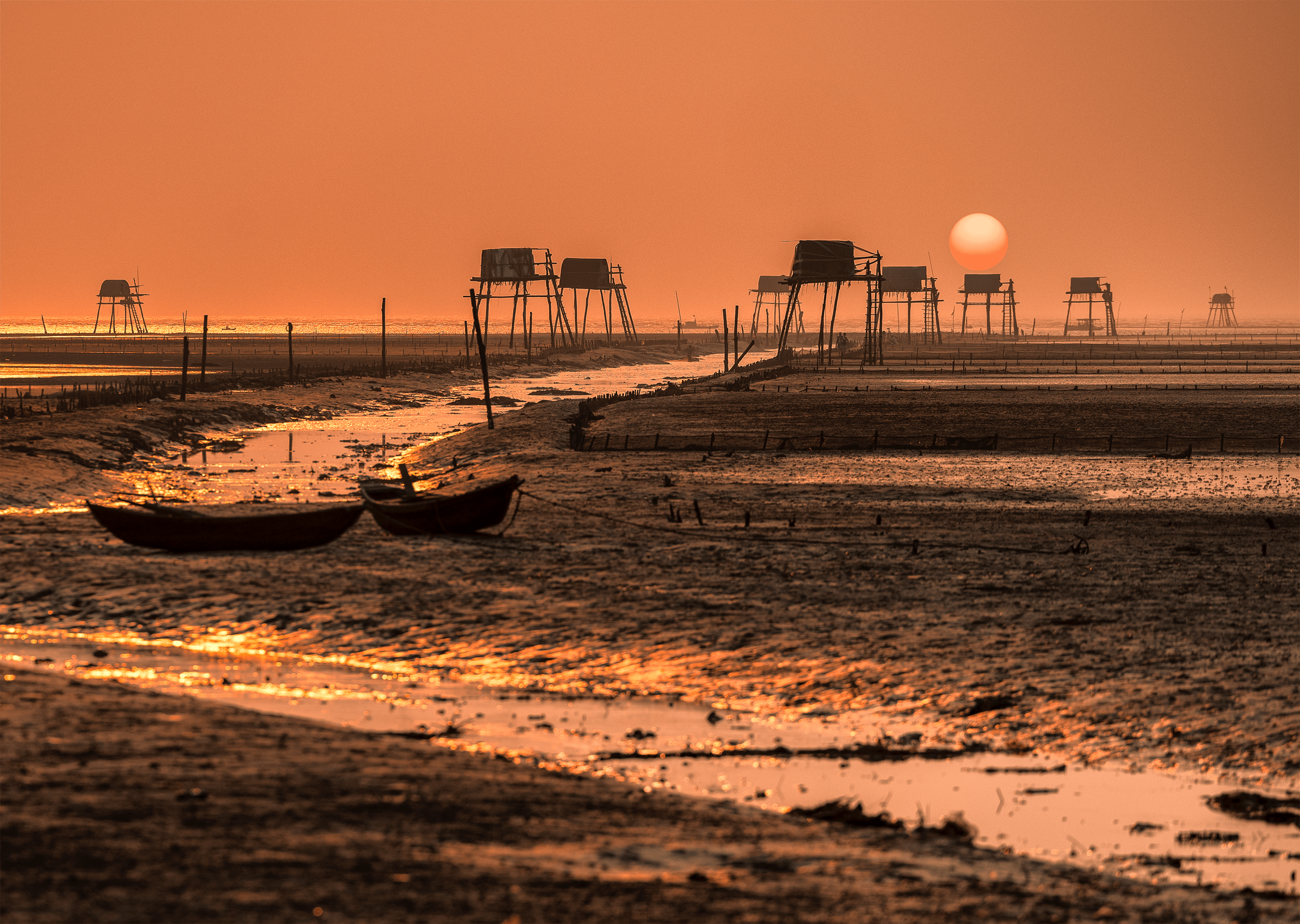 ฟรี ภาพพระอาทิตย์ตกดินอันงดงามเหนือหมู่บ้านชาวประมงที่มีเพิงไม้และเรือประมง คลังภาพถ่าย
