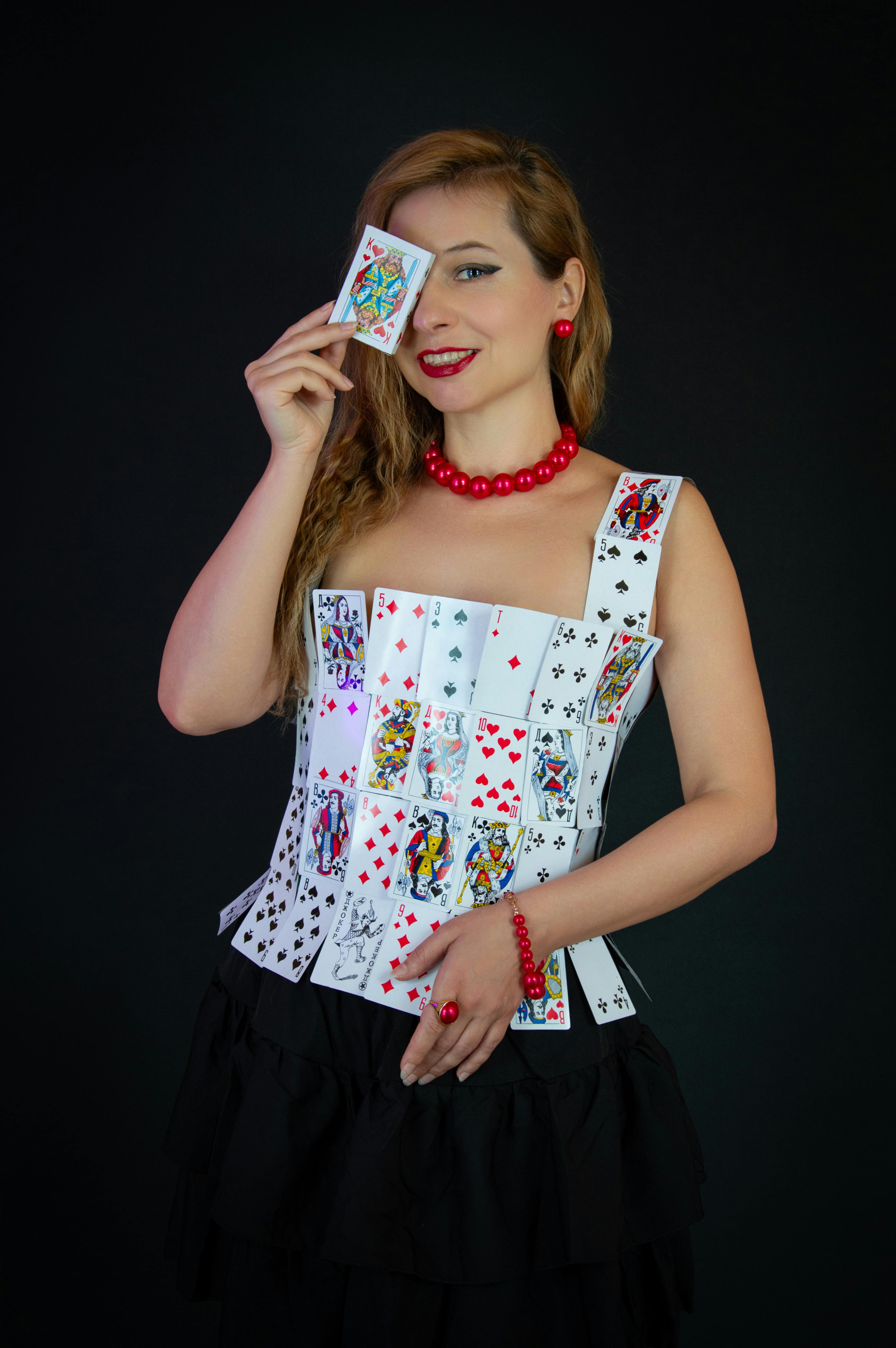 Gratuit Femeie pozând într-o rochie de cărți de joc, ținând o carte deasupra feței. Aspect elegant și artistic. Fotografie de stoc