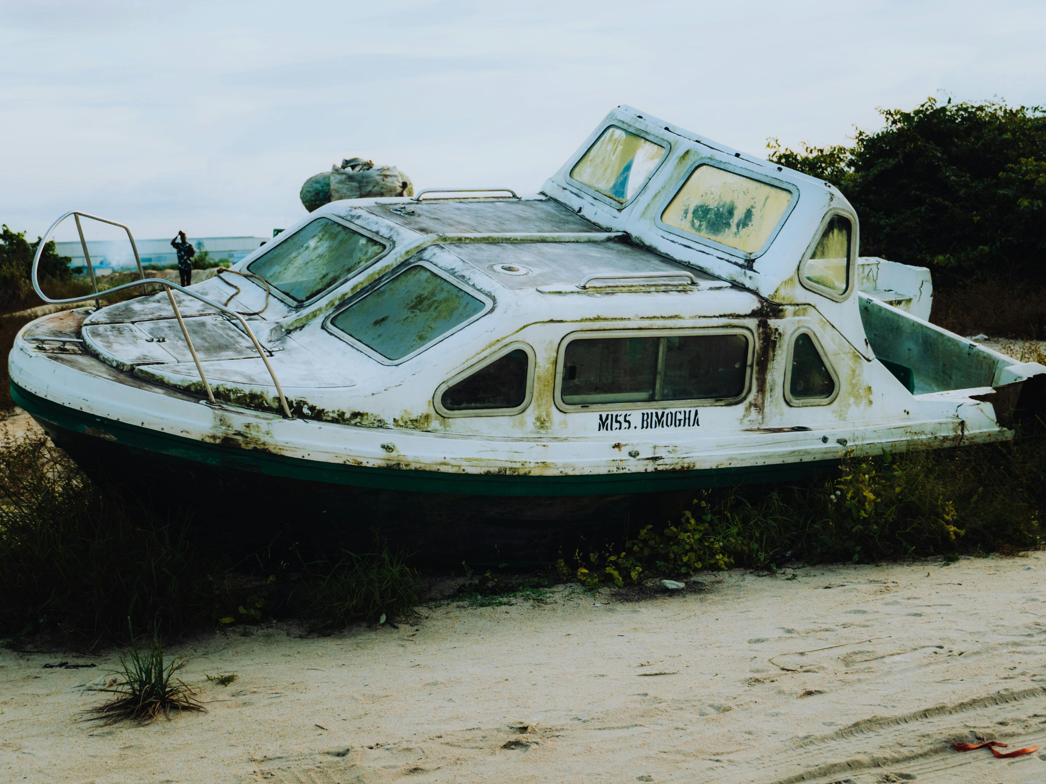 Δωρεάν Ένα παλιό, εγκαταλελειμμένο σκάφος κάθεται σε μια αμμώδη παραλία περιτριγυρισμένο από πράσινο, δημιουργώντας ένα νοσταλγικό σκηνικό. Φωτογραφία από στοκ φωτογραφιών