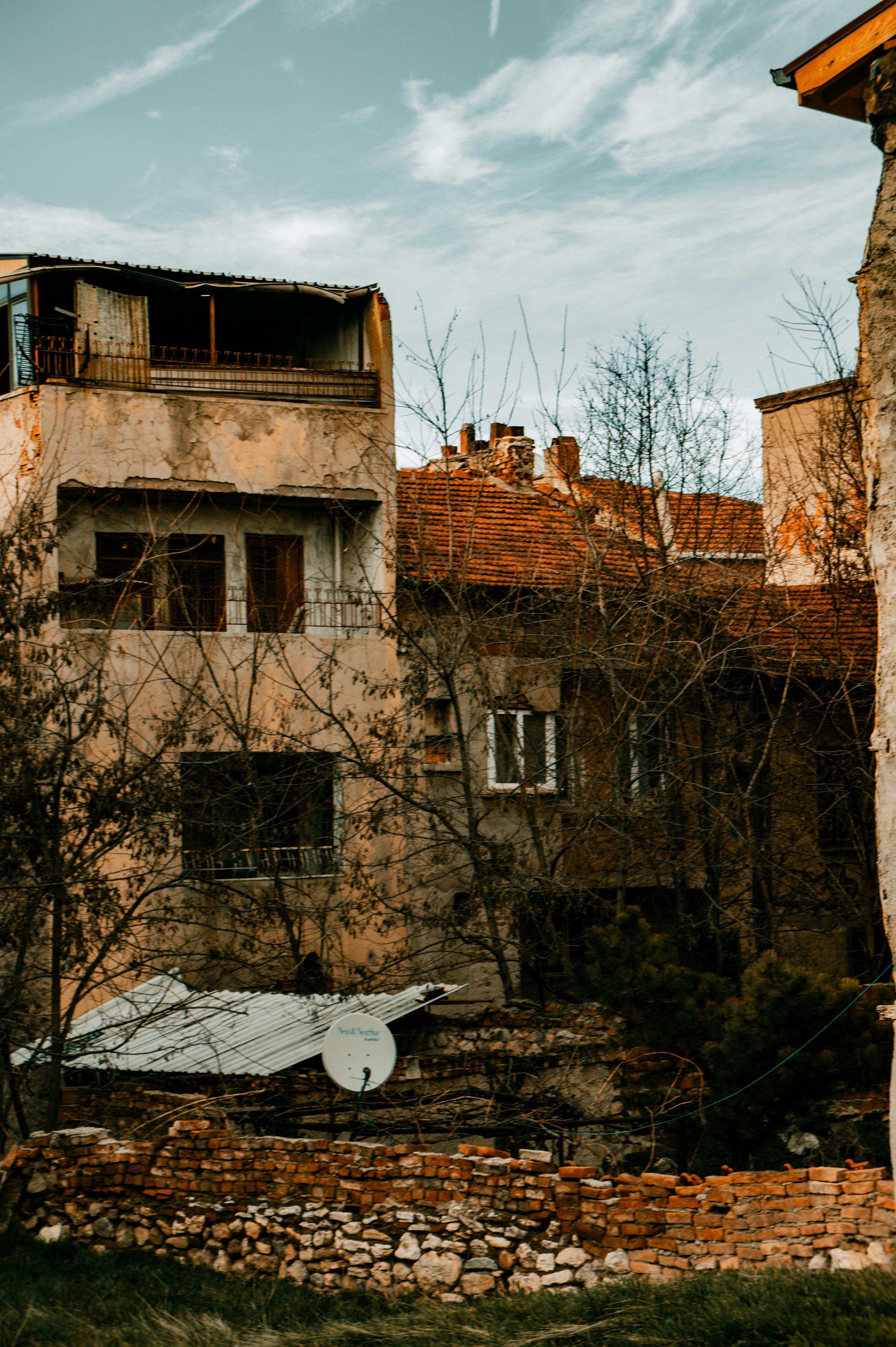 grátis Um prédio rústico e abandonado, com tijolos aparentes e antena parabólica sob um céu nublado. Foto profissional