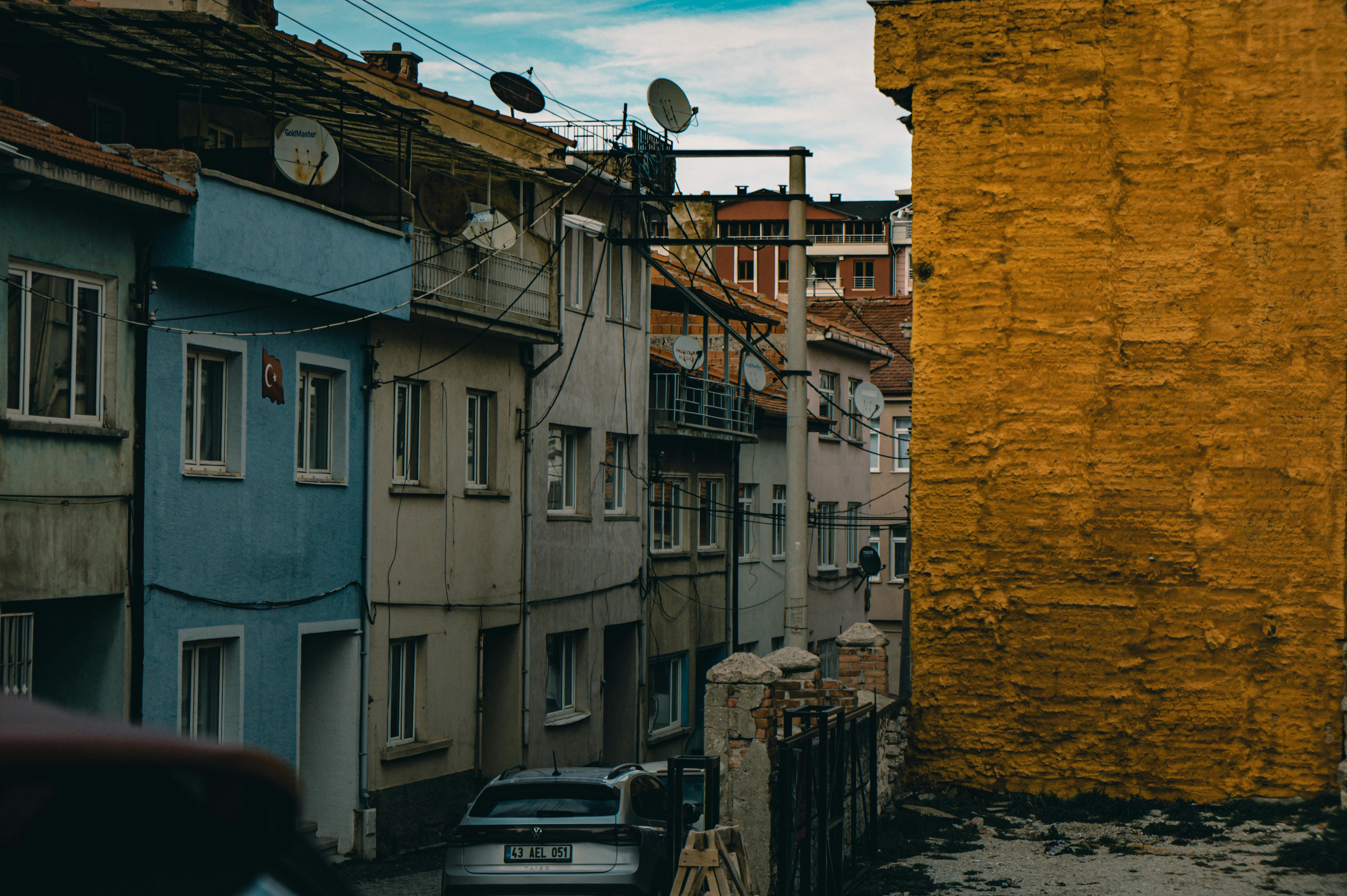 Zadarmo Úzka mestská ulička s farebnými budovami a satelitnými anténami pod jasnou oblohou. Fotka z fotobanky
