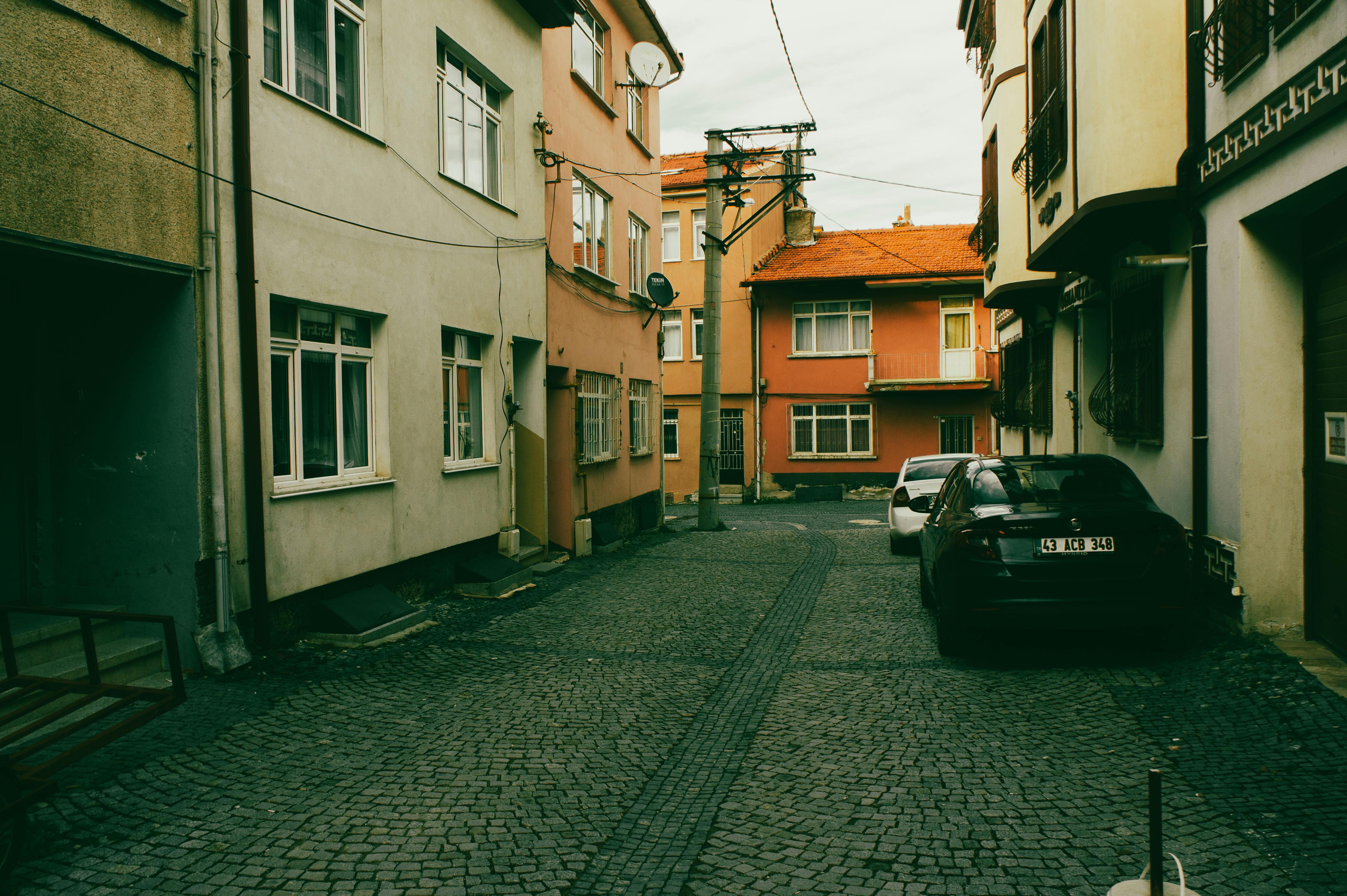 Kostnadsfria En lugn gränd med kullersten och parkerade bilar bland pastellfärgade byggnader. Stock foto