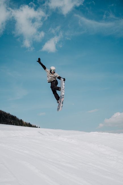 A snowboarder performs an impressive jump against a bright blue sky in the Austrian Alps.