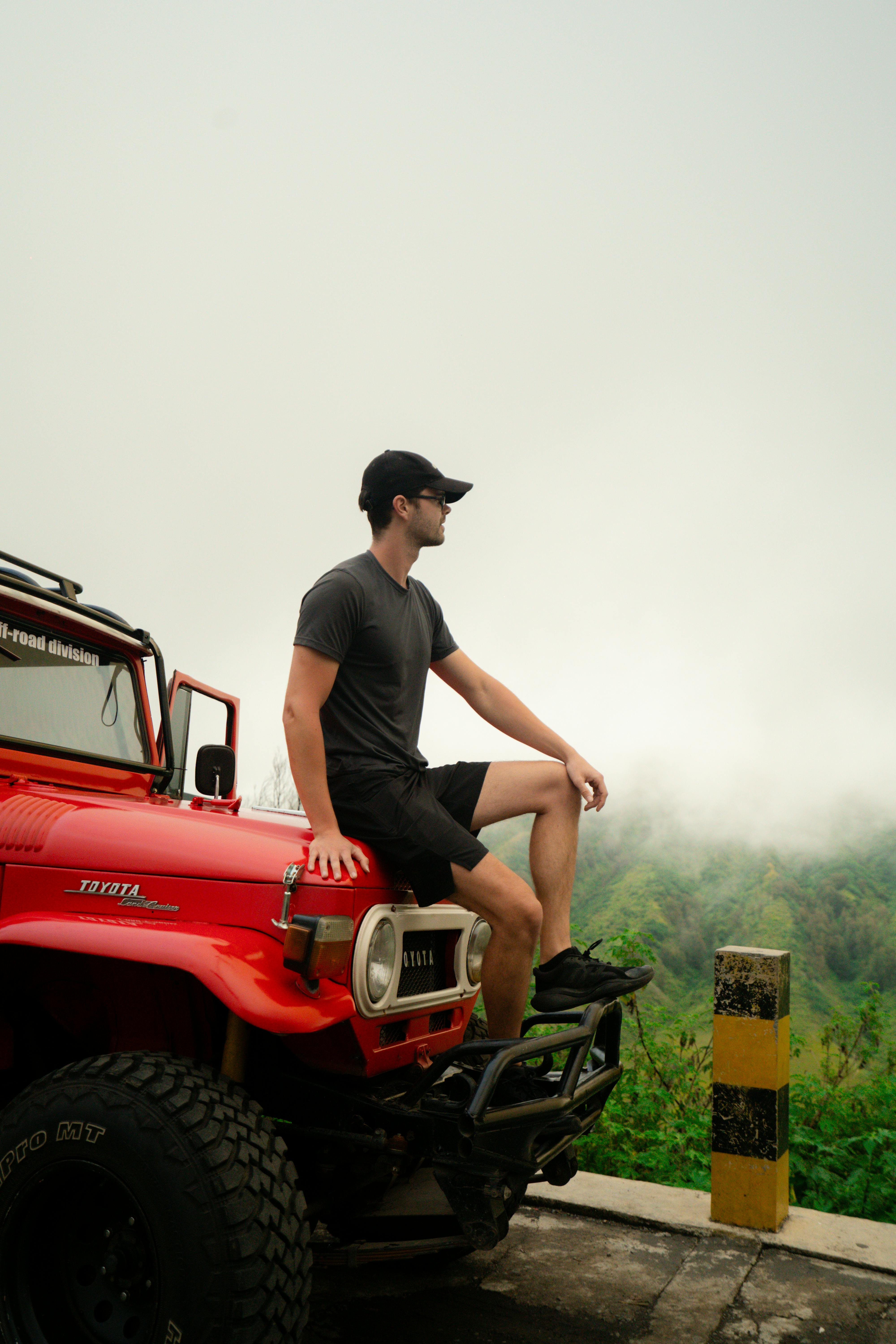 bezplatná Muž sedí v červeném džípu uprostřed mlhy a užívá si malebný výhled na hory. Základová fotografie