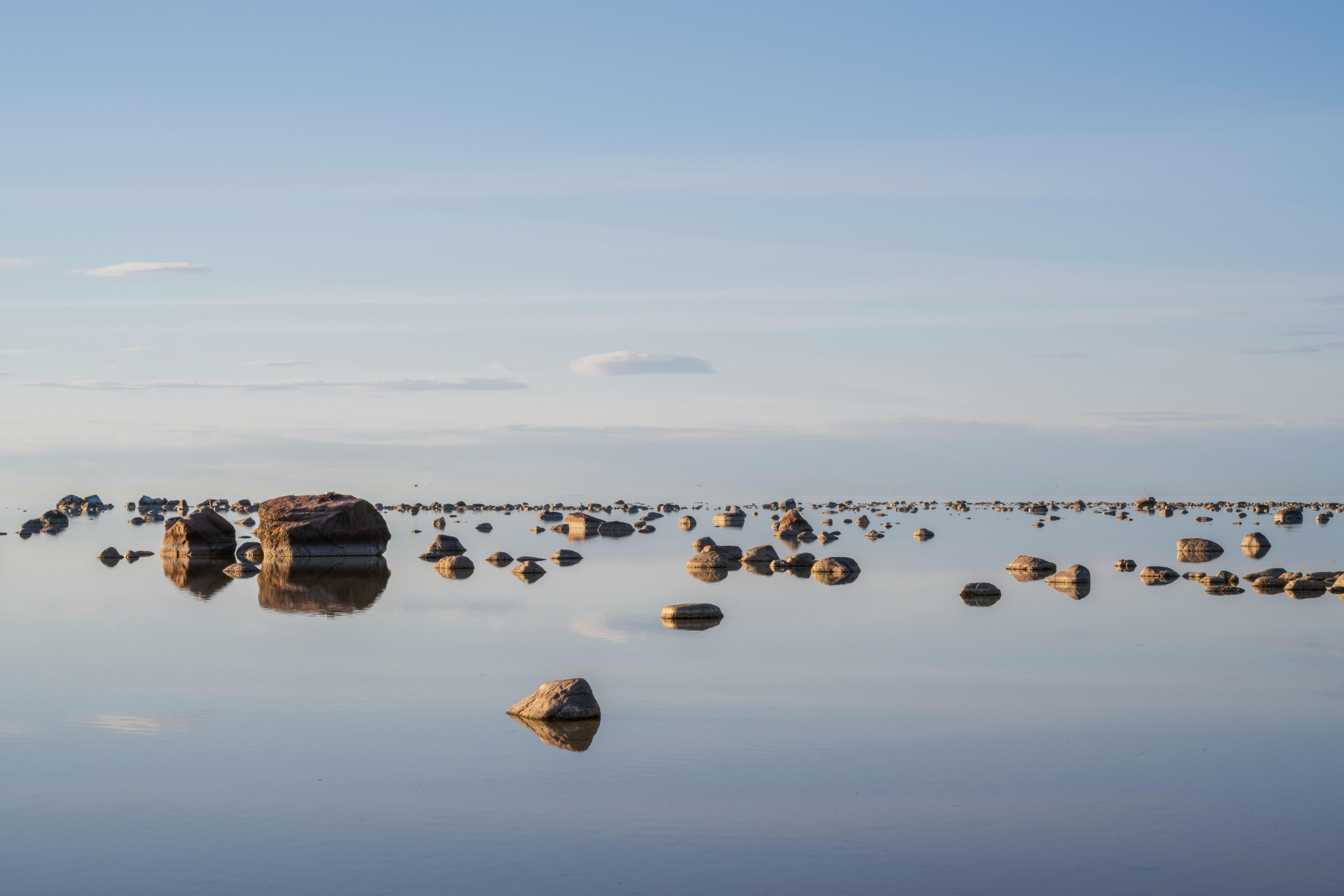 De franc Vista serena de pedres disperses en un mar tranquil sota un cel clar a la posta de sol, Estònia. Foto d'estoc