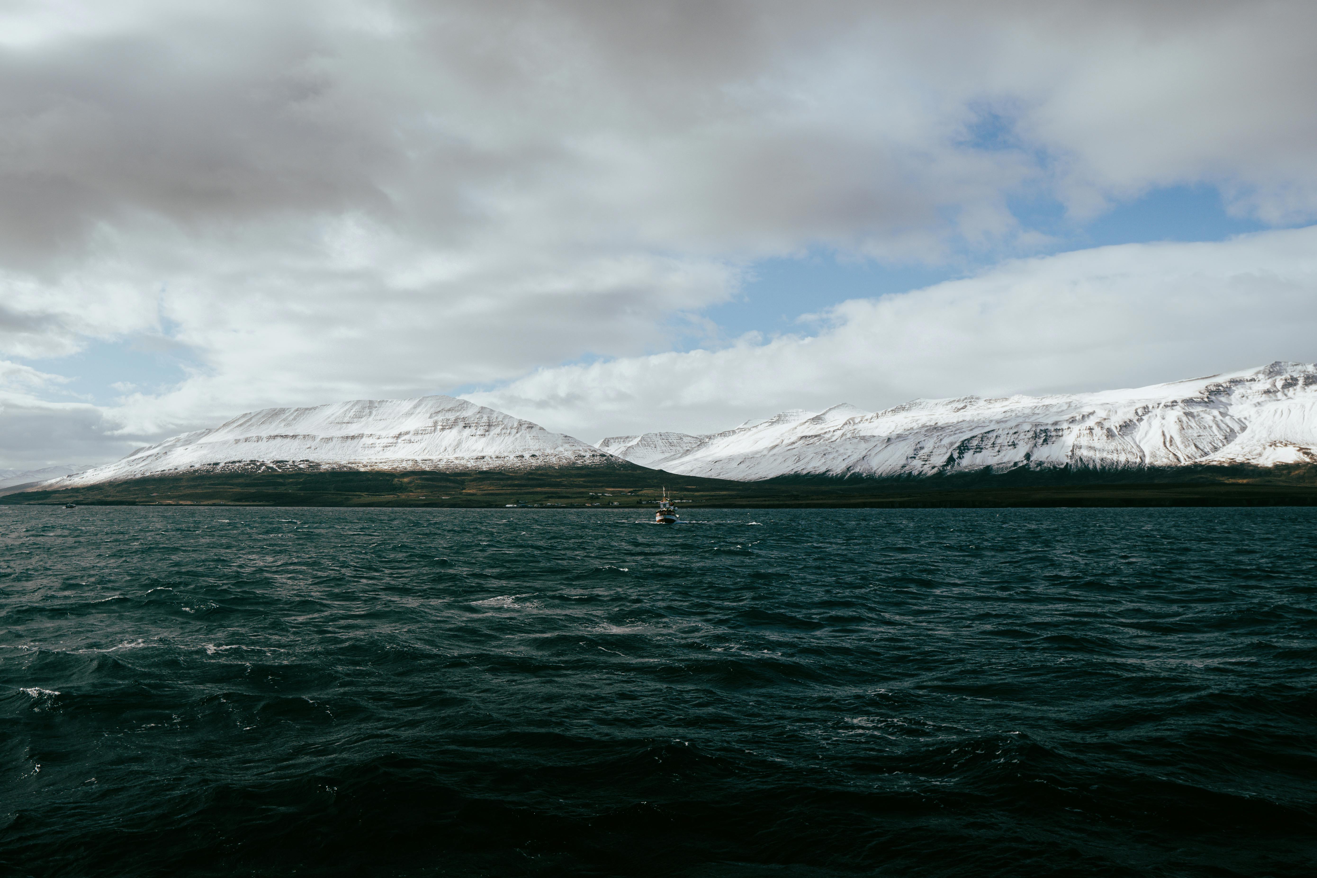 Miễn phí Một chiếc thuyền buồm lướt nhẹ trên vịnh hẹp ở Árskógssandur, Iceland, với những ngọn núi phủ đầy tuyết trắng ở phía sau. Ảnh lưu trữ
