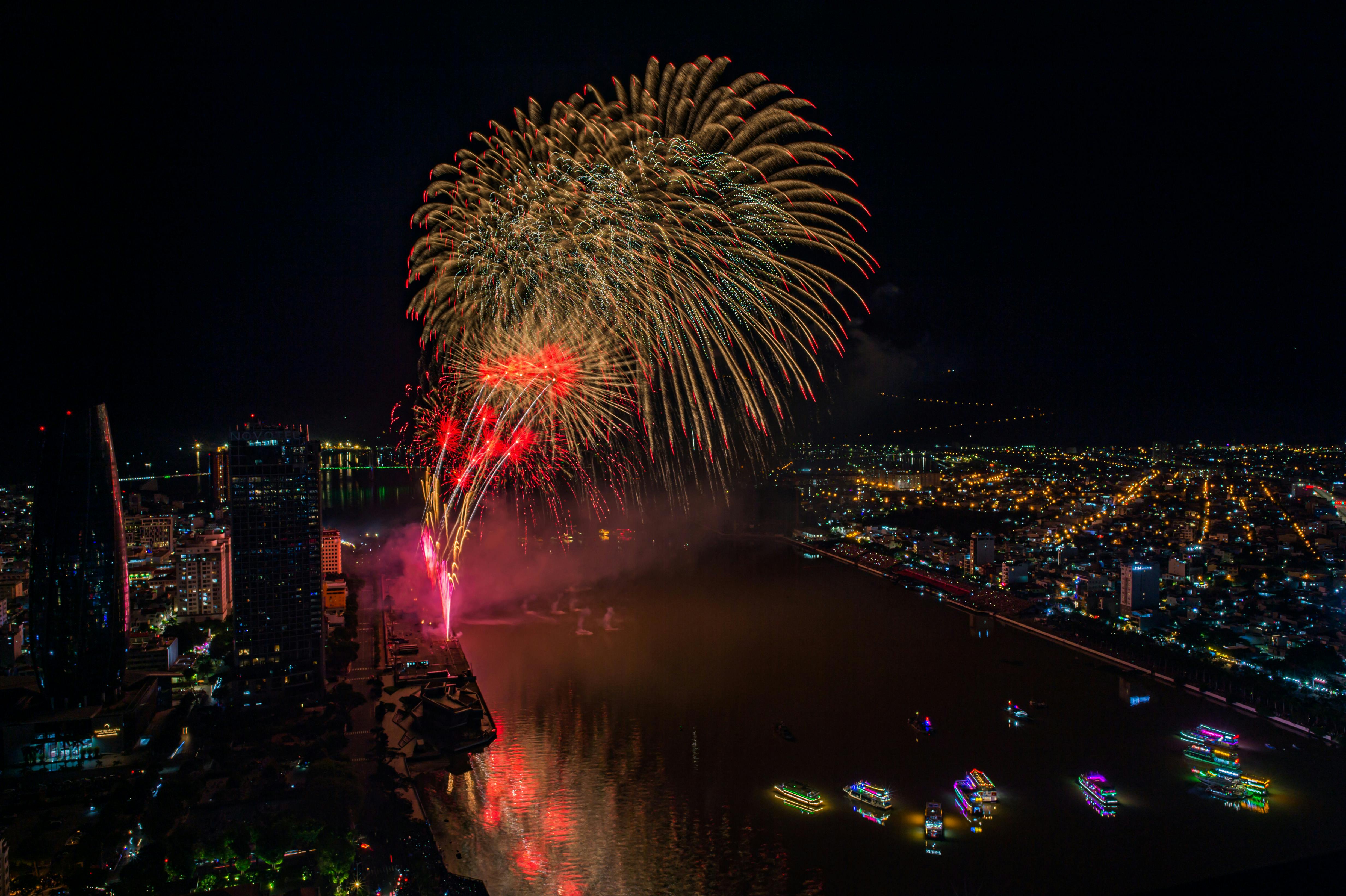 Zadarmo Žiarivé ohňostroje osvetľujúce nočnú oblohu nad mestskou krajinou odrážajúcou sa na rieke. Fotka z fotobanky
