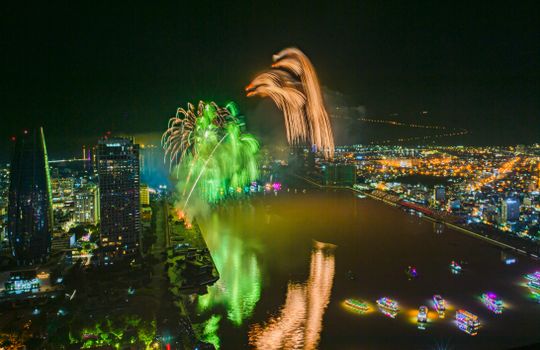Aerial view of colorful fireworks illuminating a cityscape along the river, showcasing vibrant nightlife.