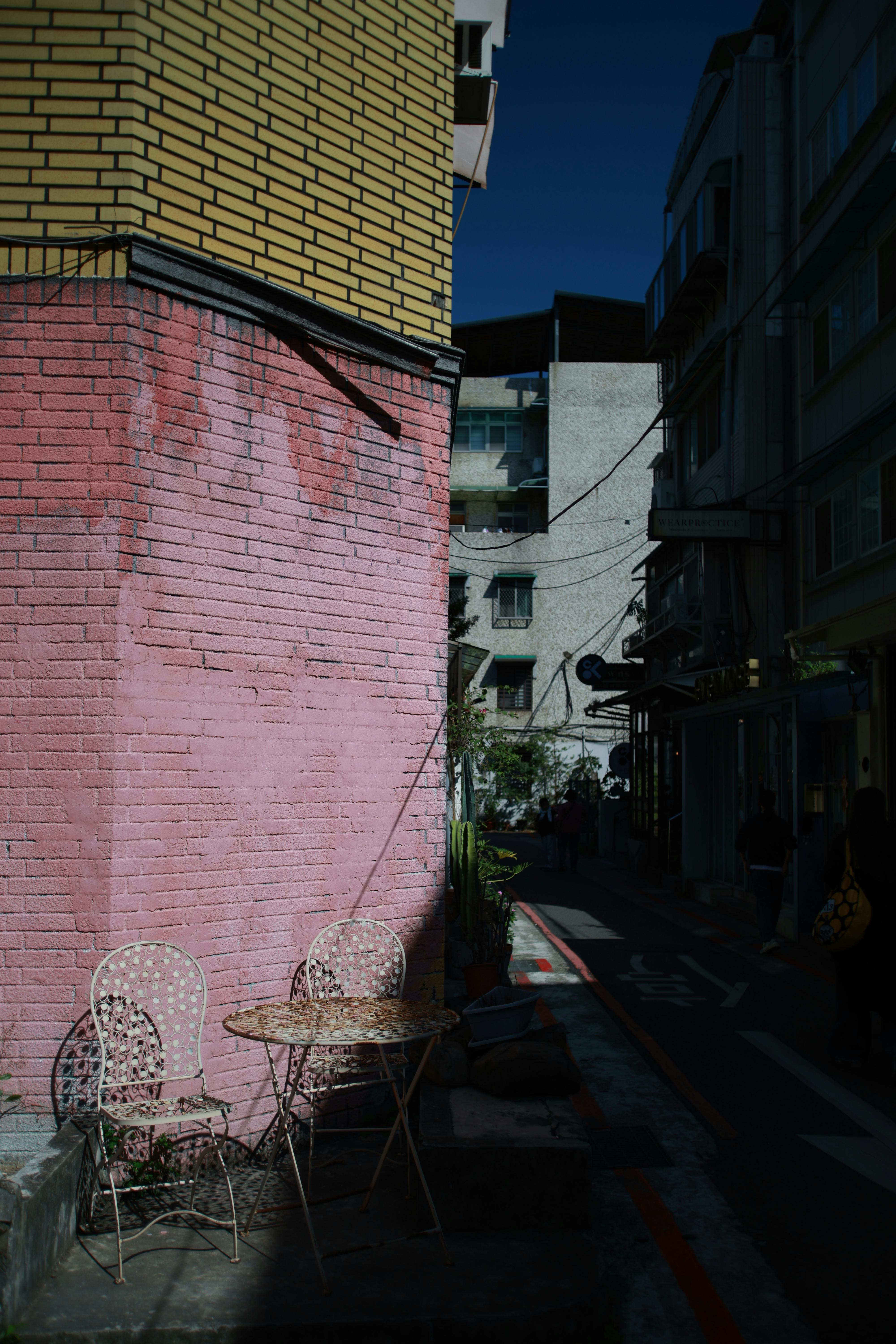Zadarmo Malebné vonkajšie prostredie s ružovou tehlovou stenou a kovovými stoličkami v tienistej uličke. Fotka z fotobanky