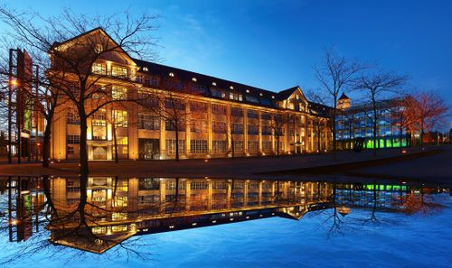 Free A beautifully lit building at night reflects in calm water, creating a stunning architectural view. Stock Photo