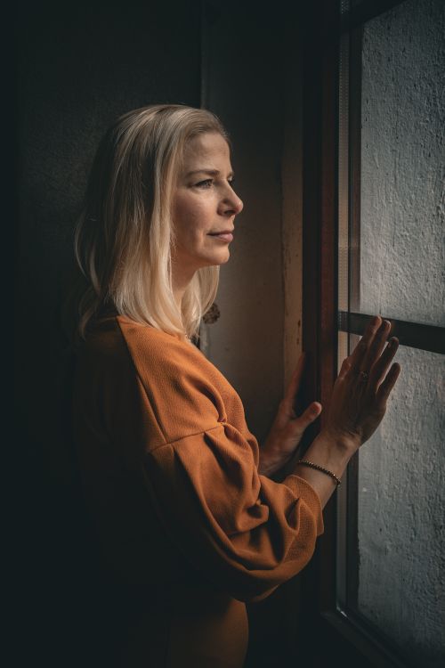 Free A contemplative woman stands by a window, bathed in warm, soft light, indoors. Stock Photo