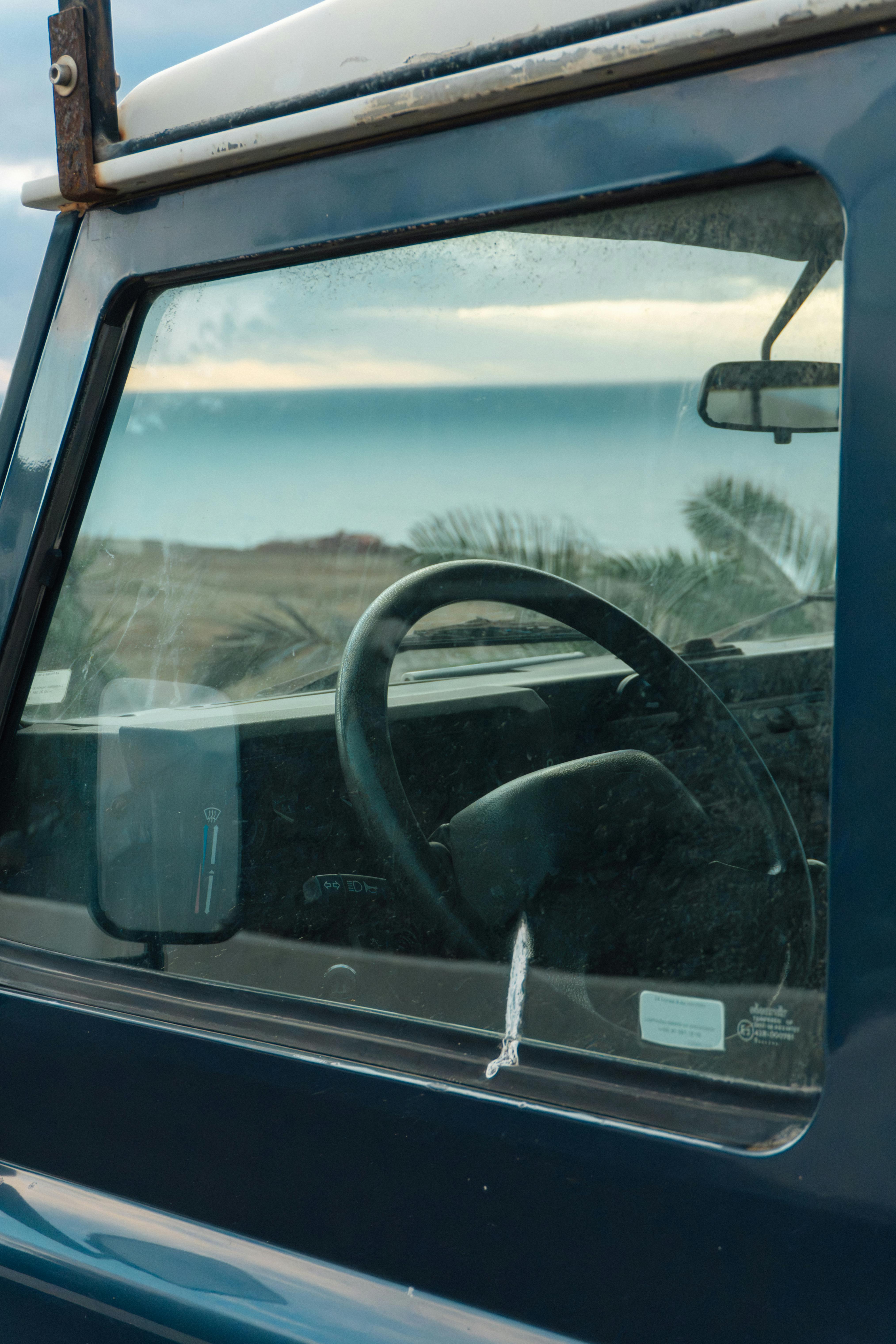 無料 海岸の風景を映し出すビンテージカーの窓。穏やかでノスタルジックな雰囲気を醸し出している。 写真素材