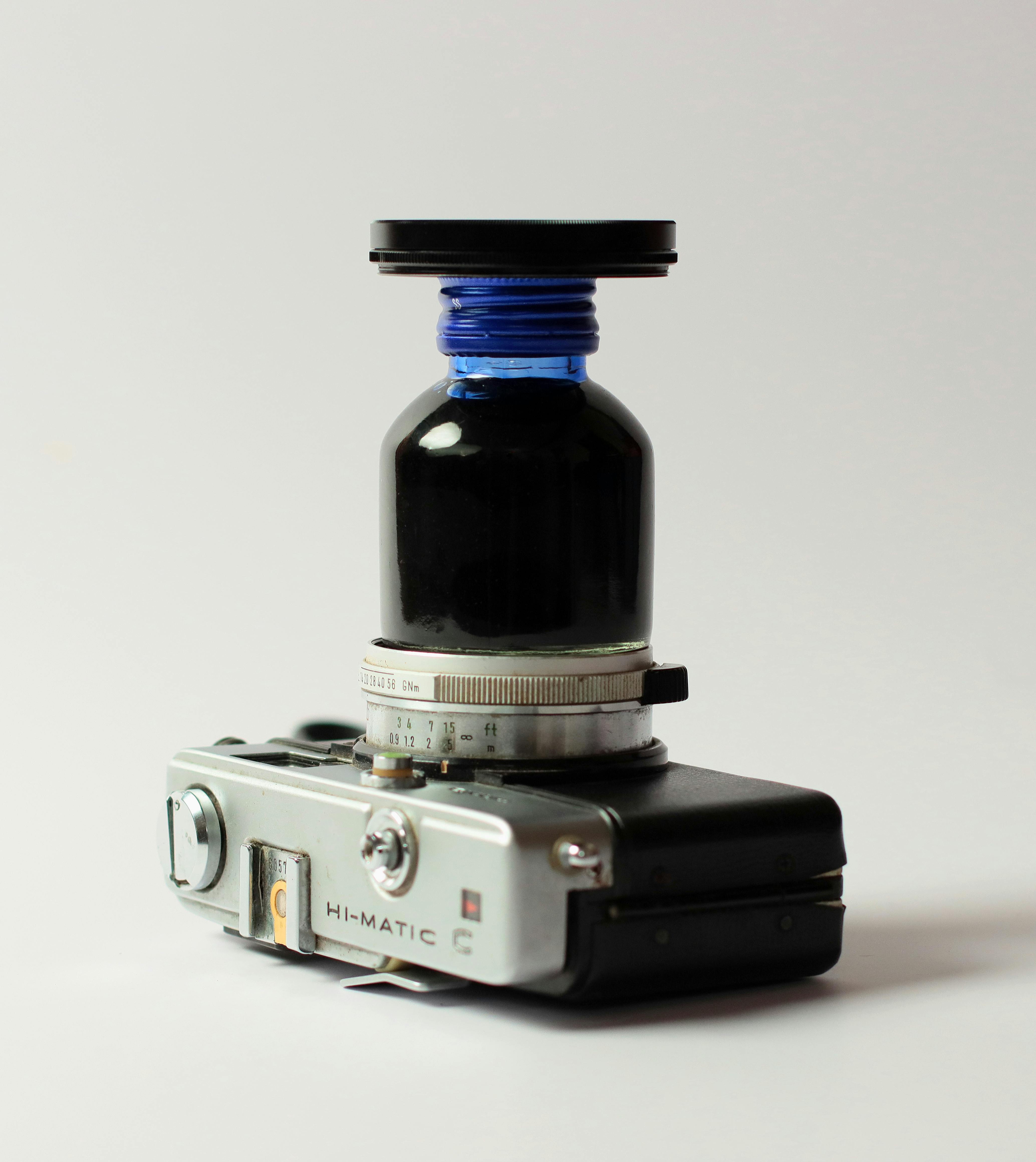 Безкоштовне Креативна композиція старовинної камери з синьою пляшкою з чорнилом як об'єктивом, ізольованою на білому. стокове фото