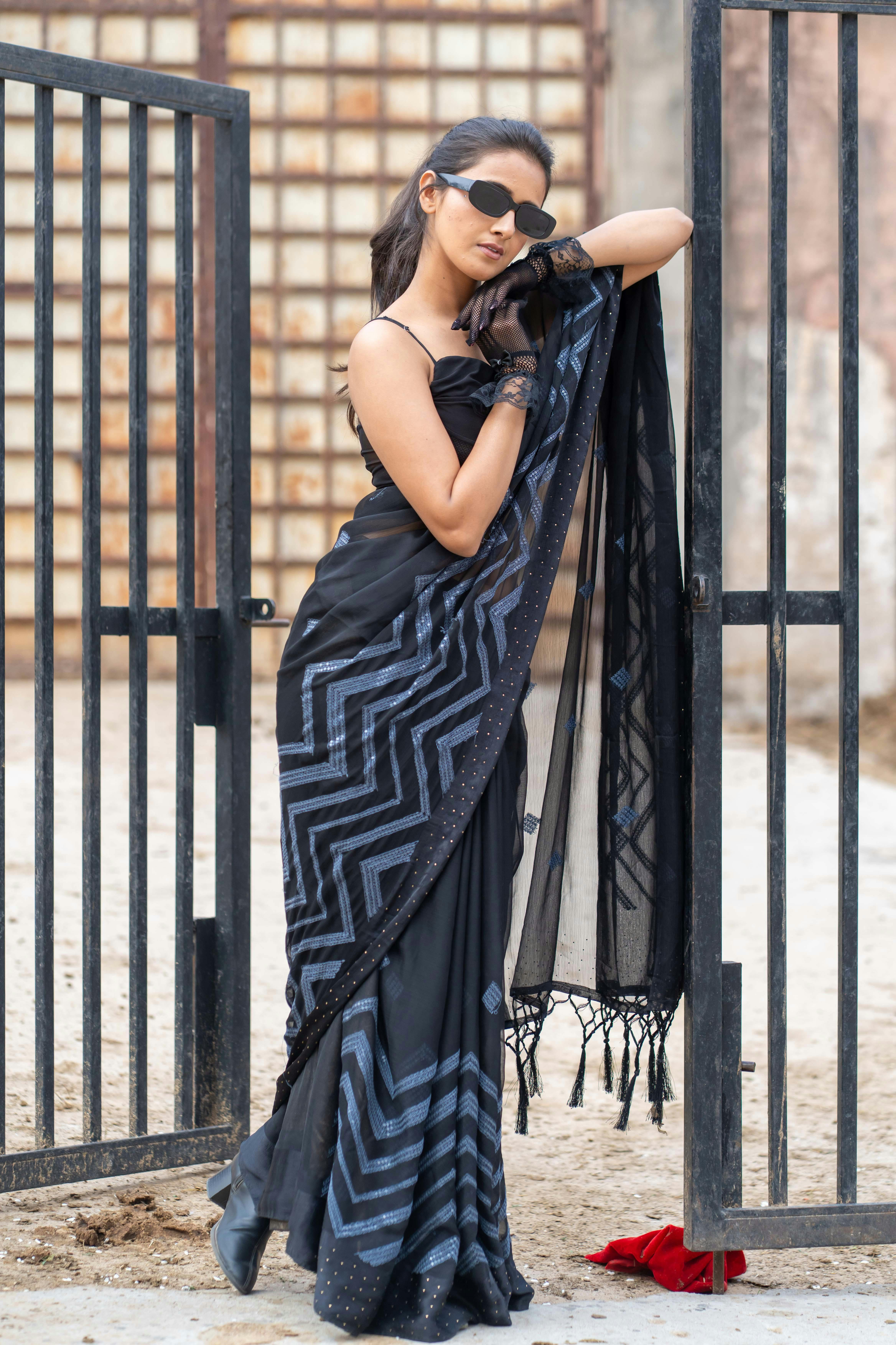 免费 一位身着黑色纱丽的时尚女子自信地站在户外大门旁。 素材图片