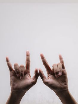 Two hands expressing a sign language gesture against a plain indoor background.