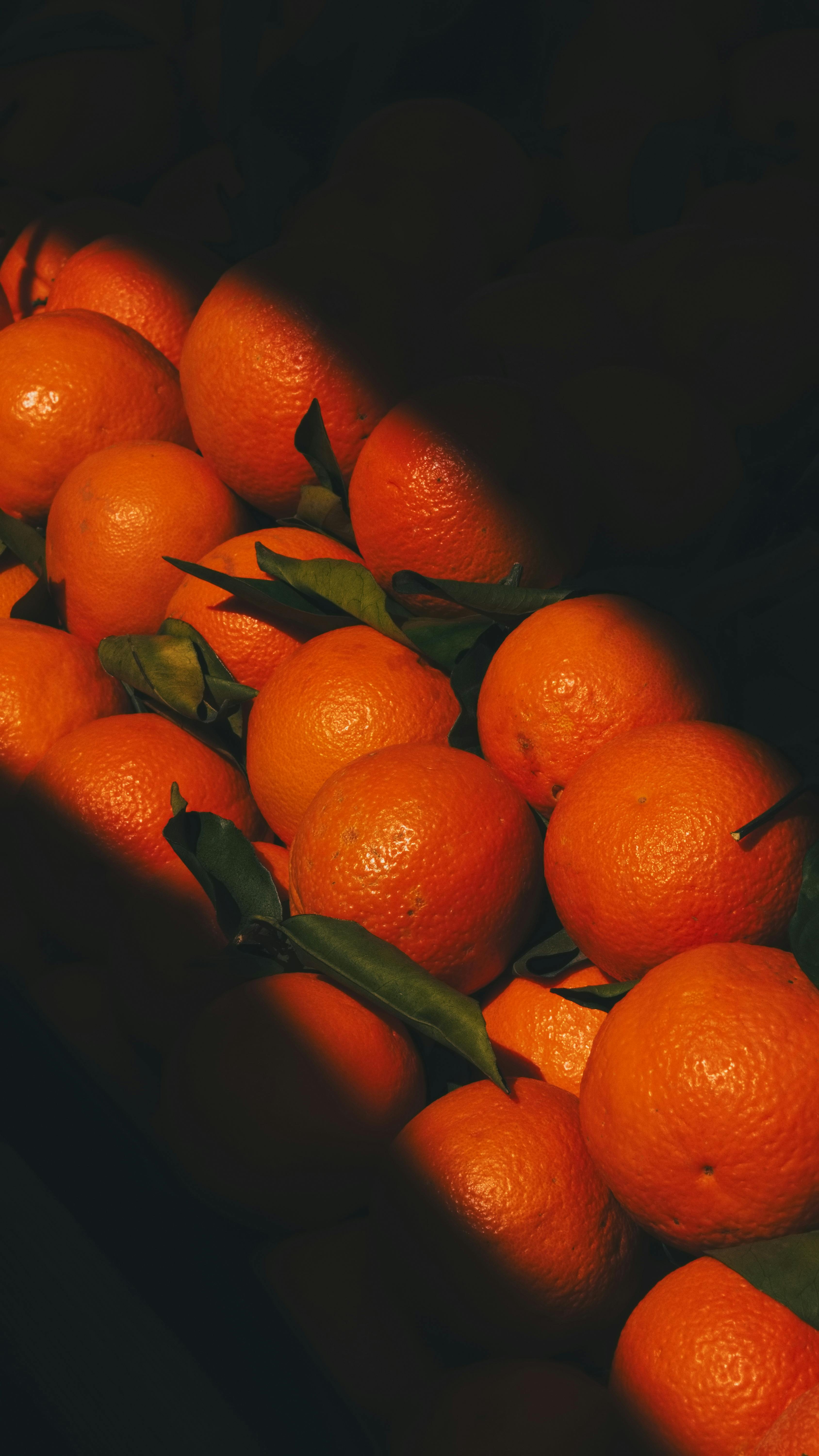 ingyenes Egy halom érett mandarin, melynek leveleit drámai megvilágítás emeli ki, gazdag, meleg hangulatot teremtve. Stockfotó