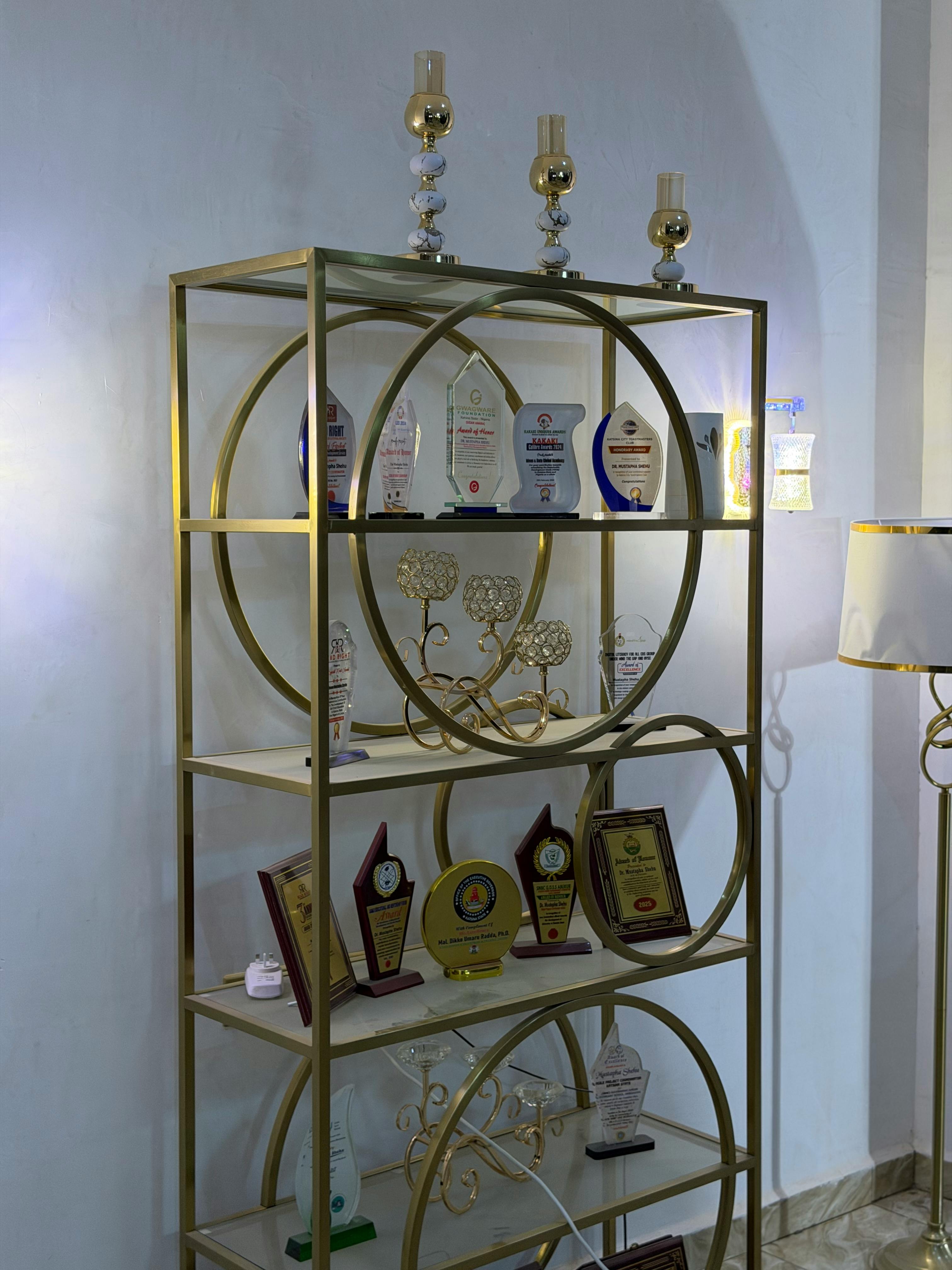 Gratis Elegante mensola dorata che espone vari trofei e premi, perfetta per arredare con stile l'ufficio o la casa. Foto a disposizione