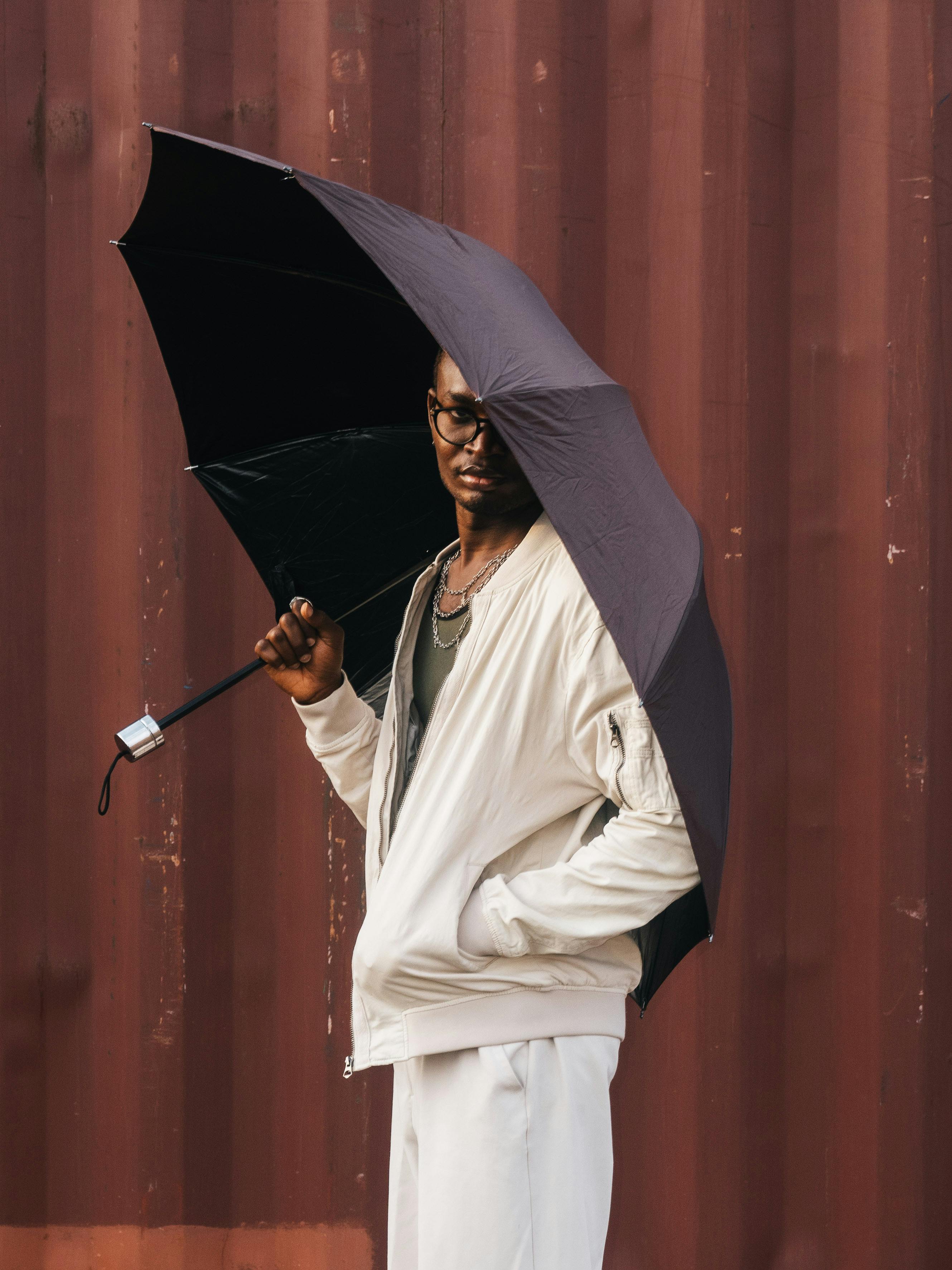 ฟรี ชายหนุ่มแต่งตัวทันสมัยยืนอยู่กลางแจ้งพร้อมร่มในเมืองอาบูจา ประเทศไนจีเรีย คลังภาพถ่าย