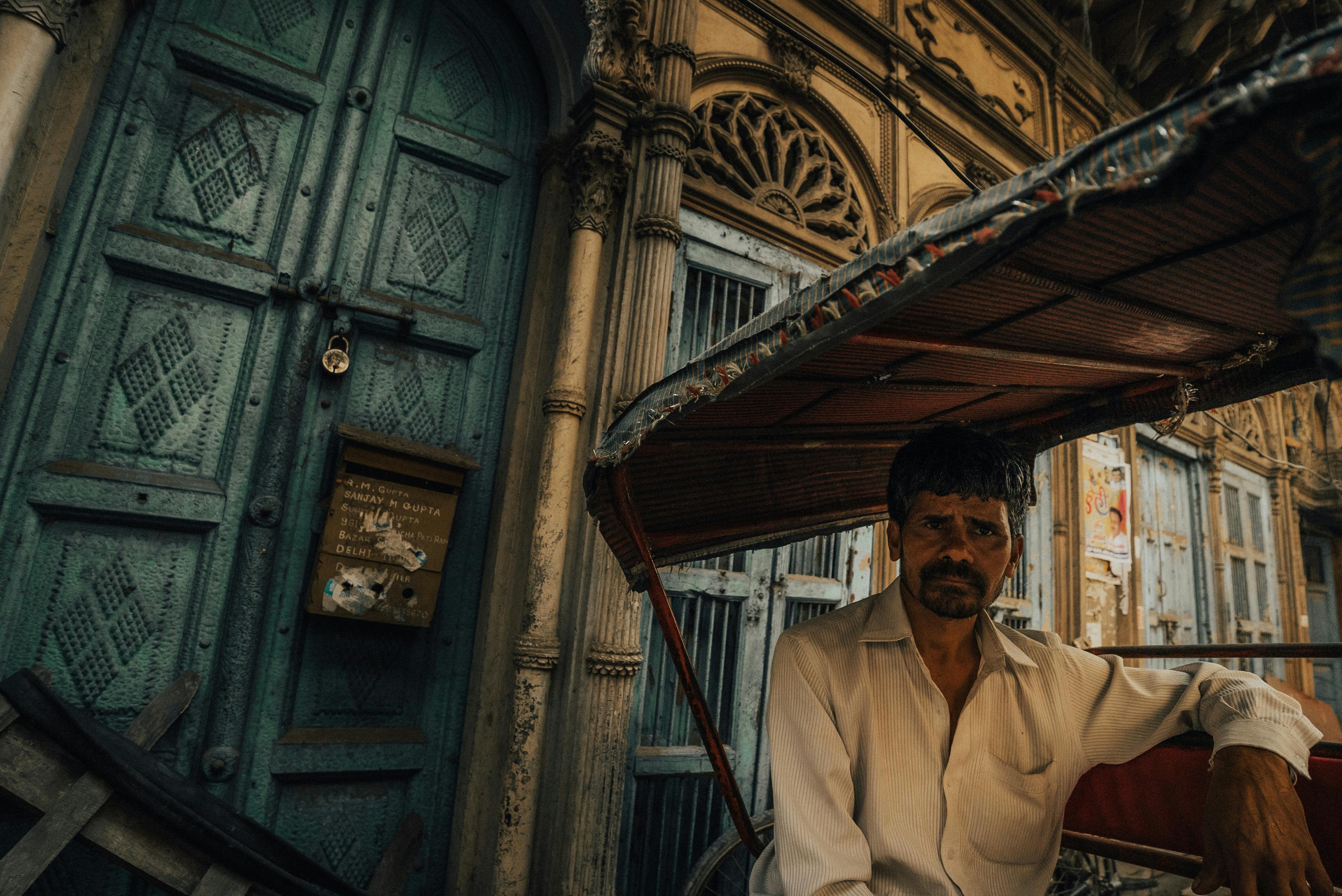 Zadarmo Portrét vodiča rikši na pozadí starej ulice v Dillí s historickou architektúrou. Fotka z fotobanky