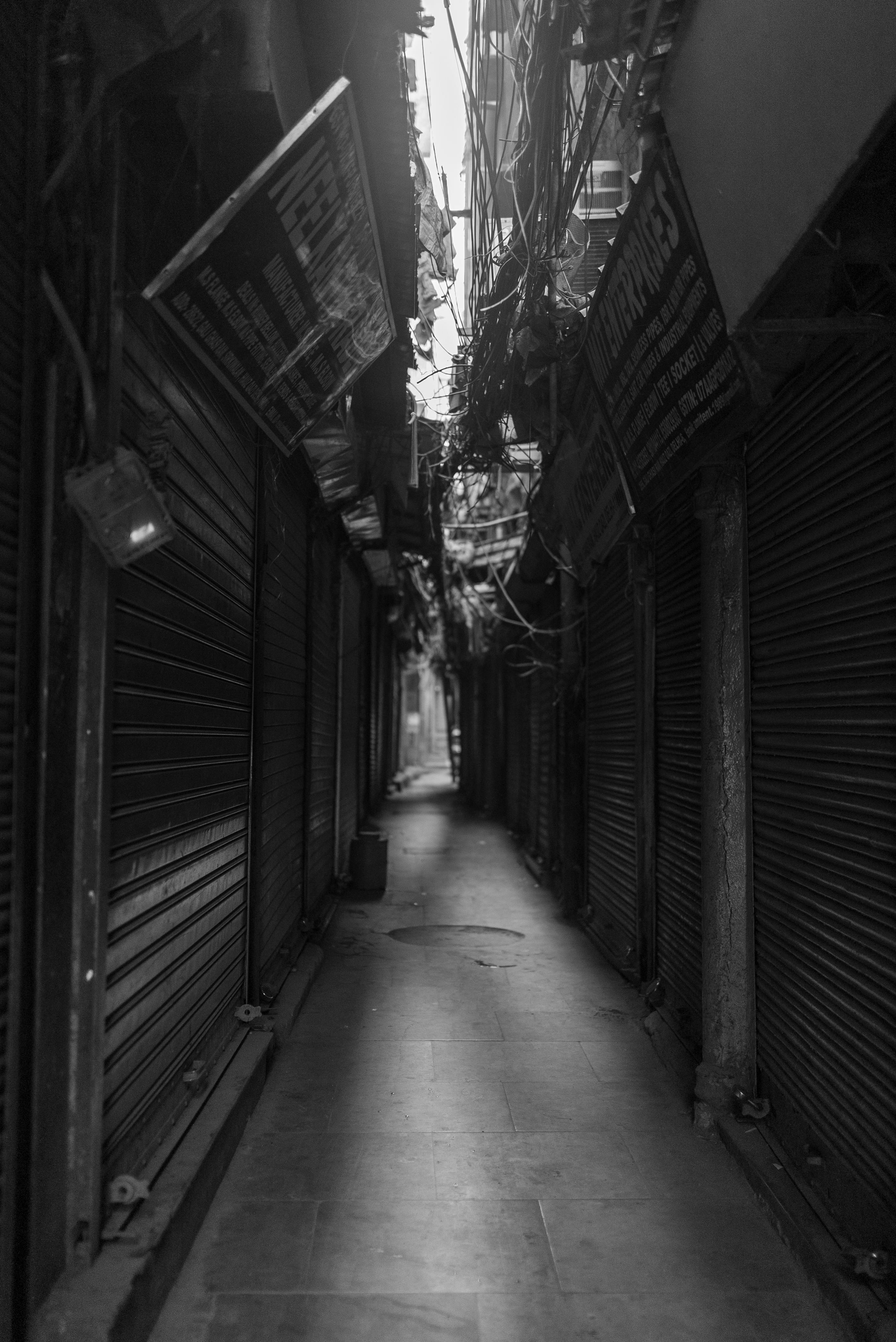 무료 좁고 인적 없는 골목길은 그림자에 휩싸여 있고, 닫힌 금속 셔터와 머리 위로 드리워진 전선들이 눈에 띈다. 스톡 사진