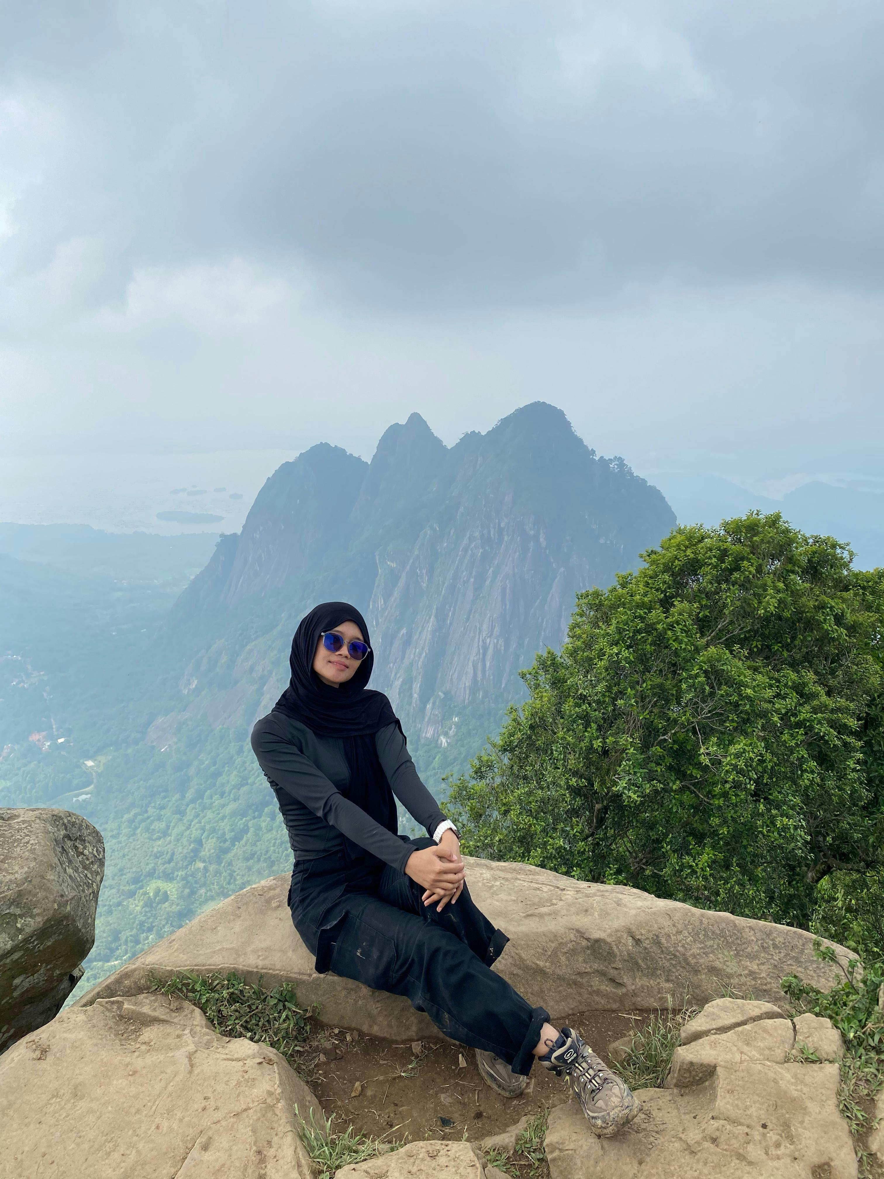 Gratis Donna seduta su una roccia con una vista panoramica sulle montagne sullo sfondo. Foto a disposizione