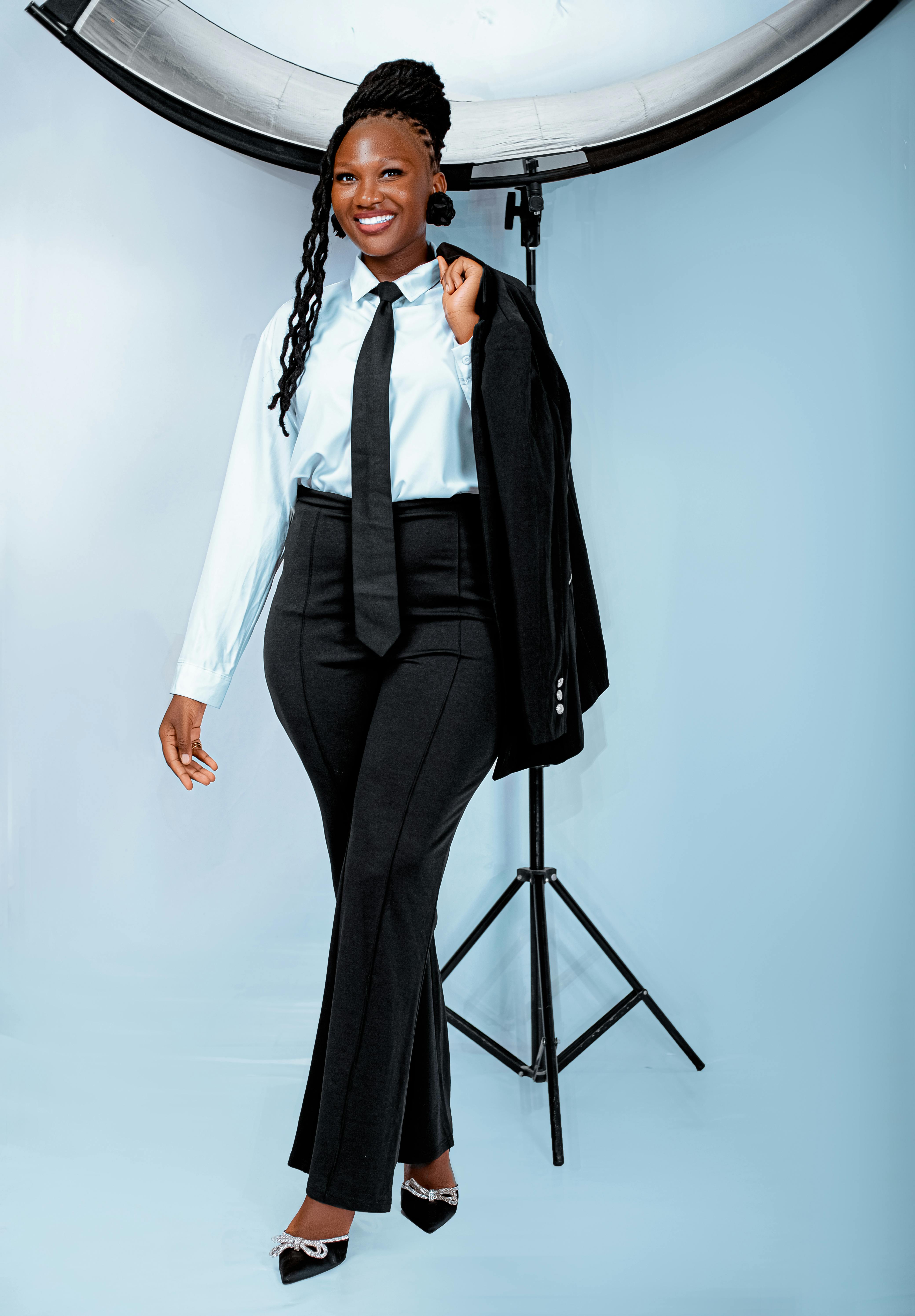 Gratis Selvsikker kvinde i jakkesæt poserer med et smil mod en baggrund i et studie. Lagerfoto