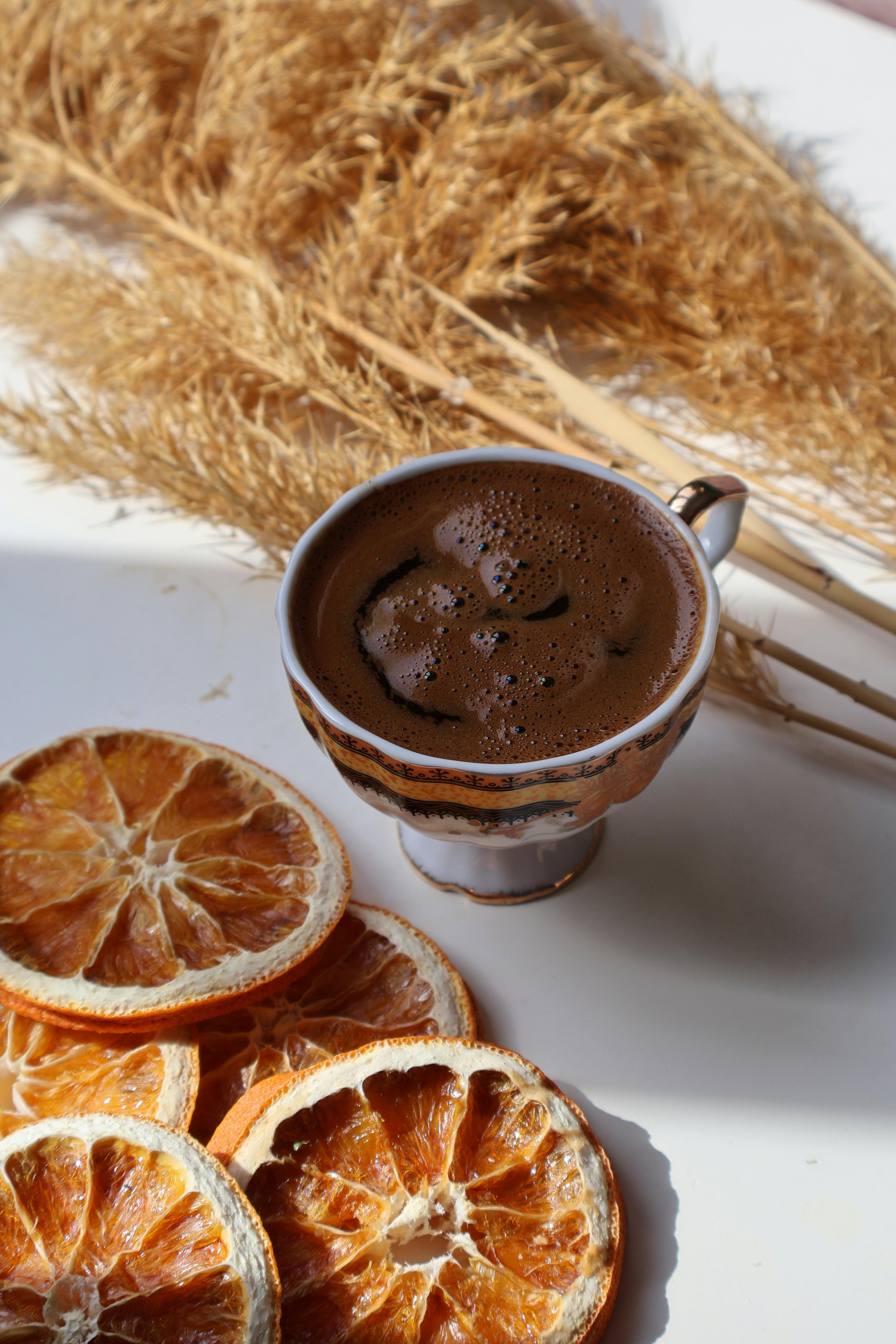 Gratis Accogliente tazza da caffè con fette d'arancia essiccate ed erba della pampa in un ambiente caldo e rustico. Foto a disposizione