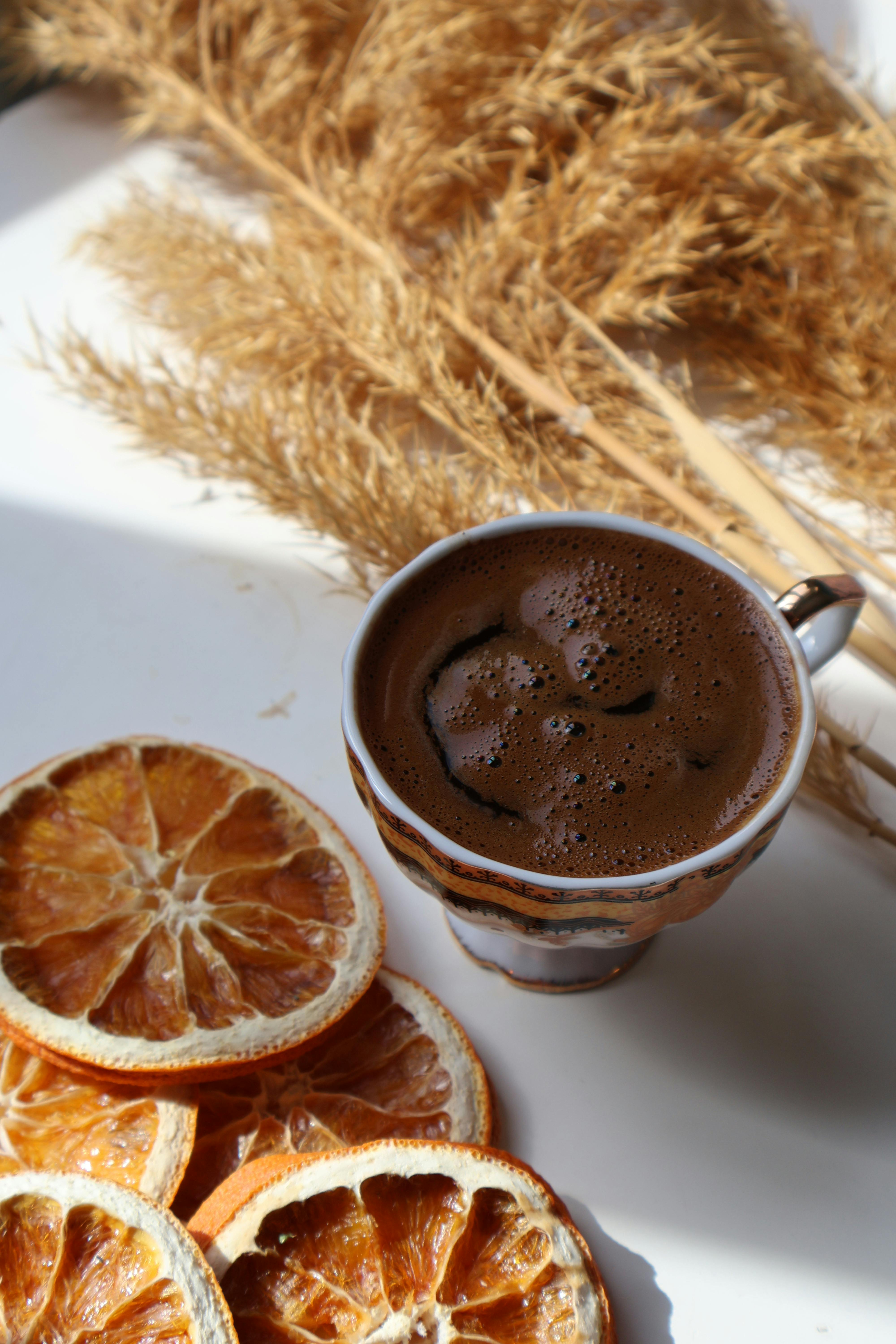 Gratis Un'accogliente composizione con una tazza di caffè, arance essiccate e spighe di grano nella luce soffusa del sole. Foto a disposizione
