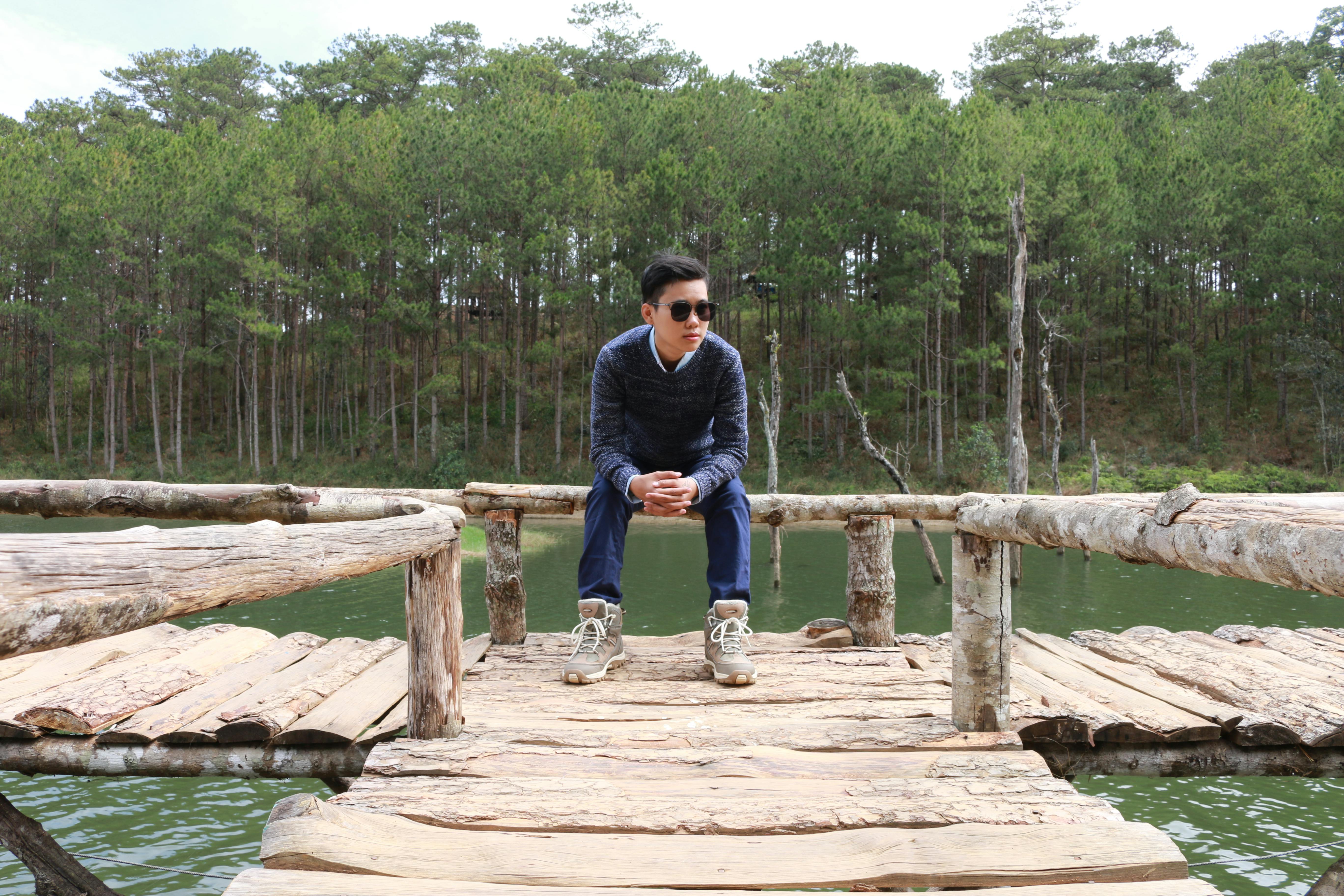 bezplatná Stylový muž pózuje na dřevěném mostě přes klidné jezero v prostředí borového lesa. Základová fotografie