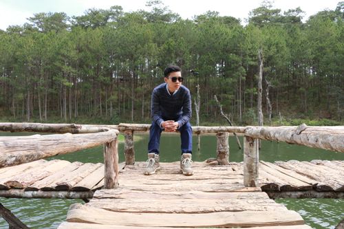 Free A stylish man poses on a wooden bridge over a serene lake in a pine forest setting. Stock Photo