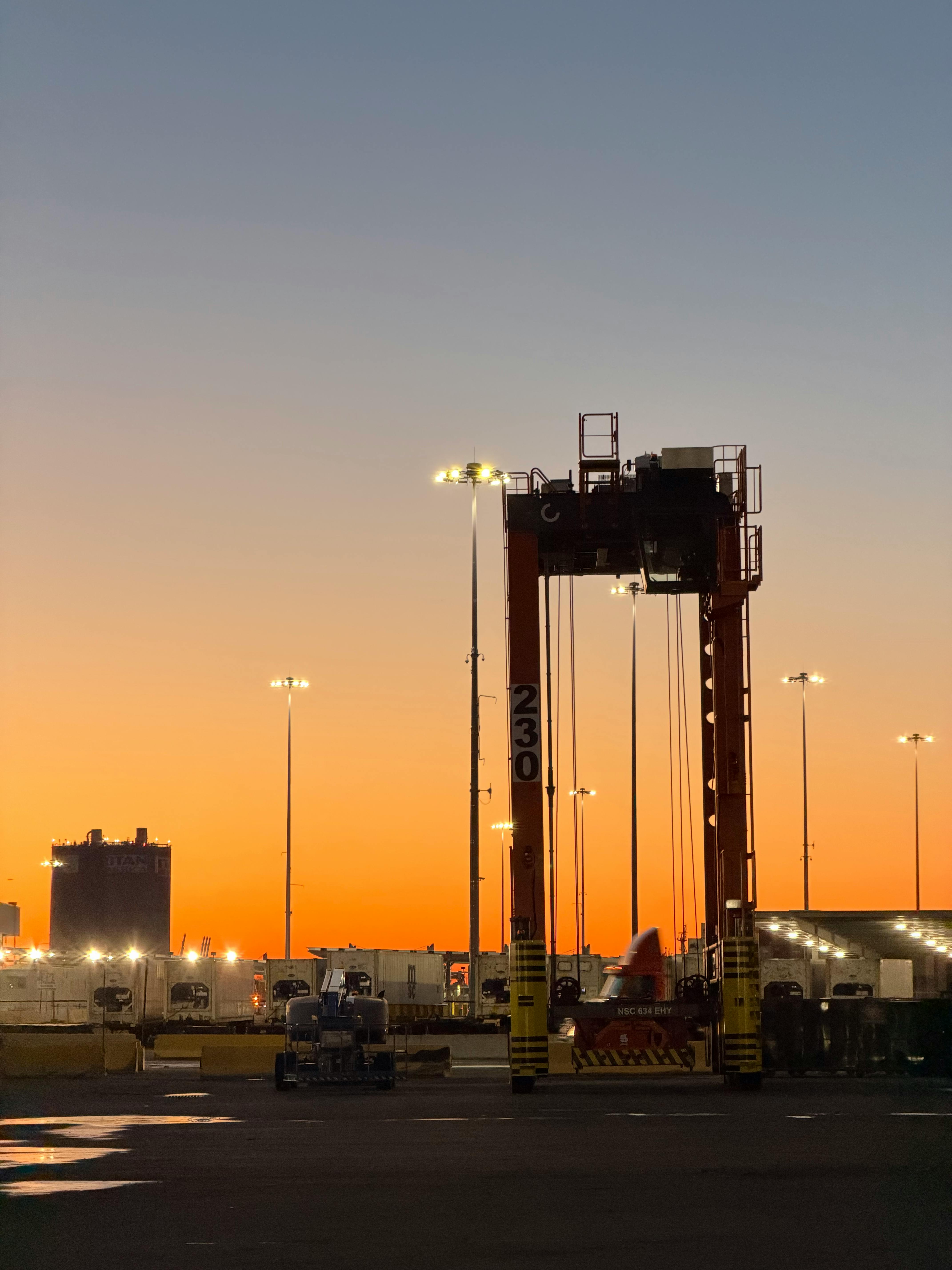 Gratuit Terminal portuaire industriel avec grue au coucher du soleil, capturant une scène crépusculaire urbaine. Photos