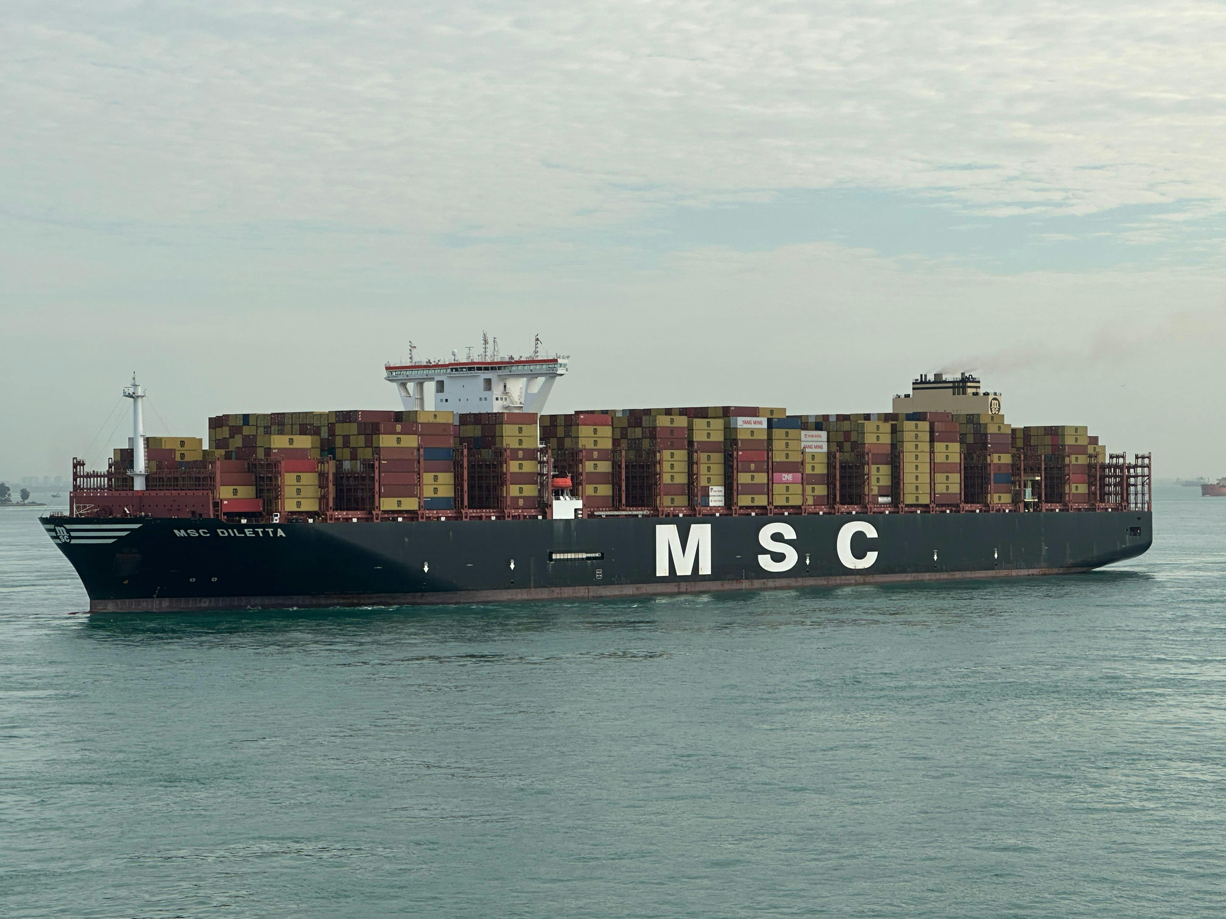 無料 積み上げられたコンテナを積んだMSC貨物船が、曇り空の下、外洋を航行している。 写真素材