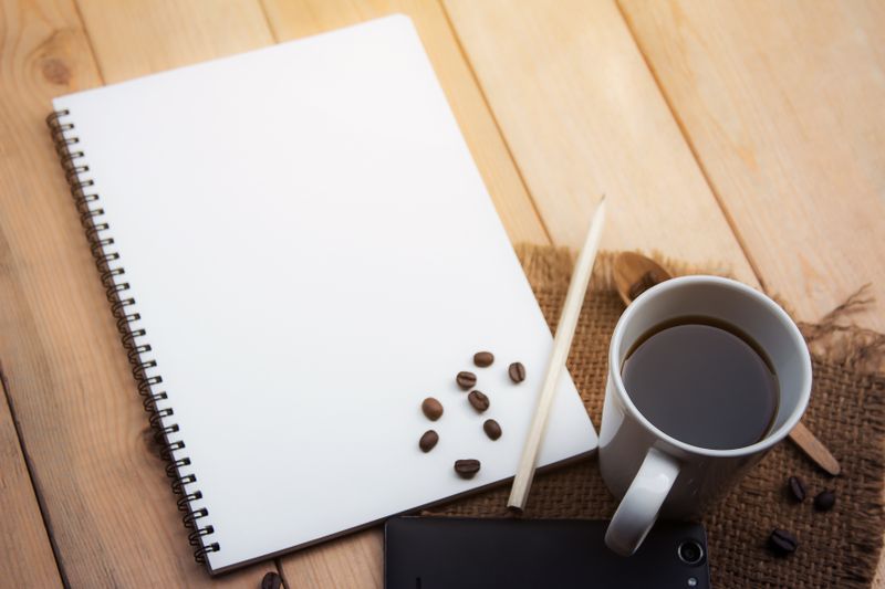 Notebook and coffee cup with a pencil on a wooden desk