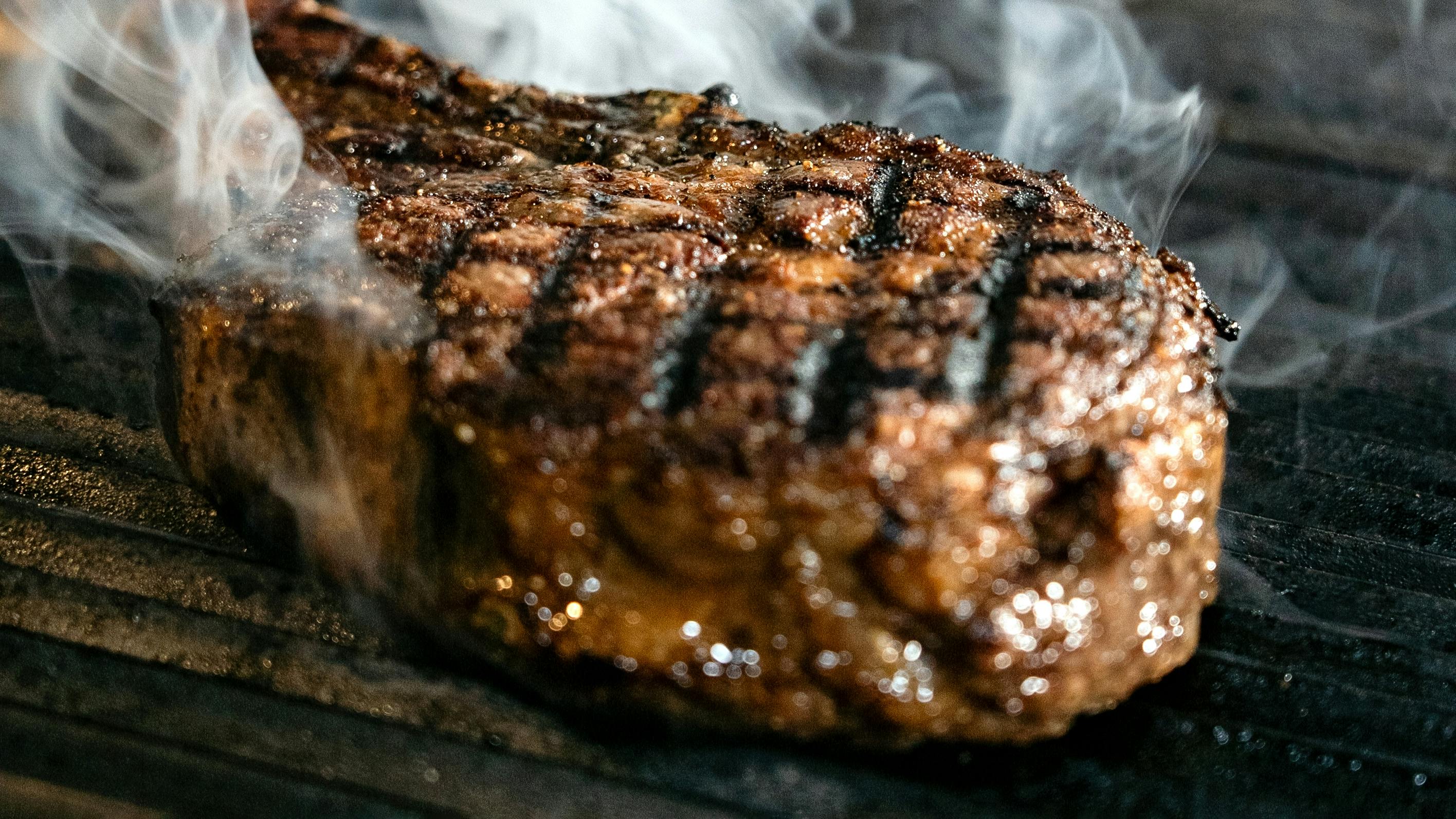 Kostenlos Nahaufnahme eines gegrillten Steaks, aus dem Rauch aufsteigt, wodurch seine saftige Textur und die Grillstreifen hervorgehoben werden. Stock-Foto