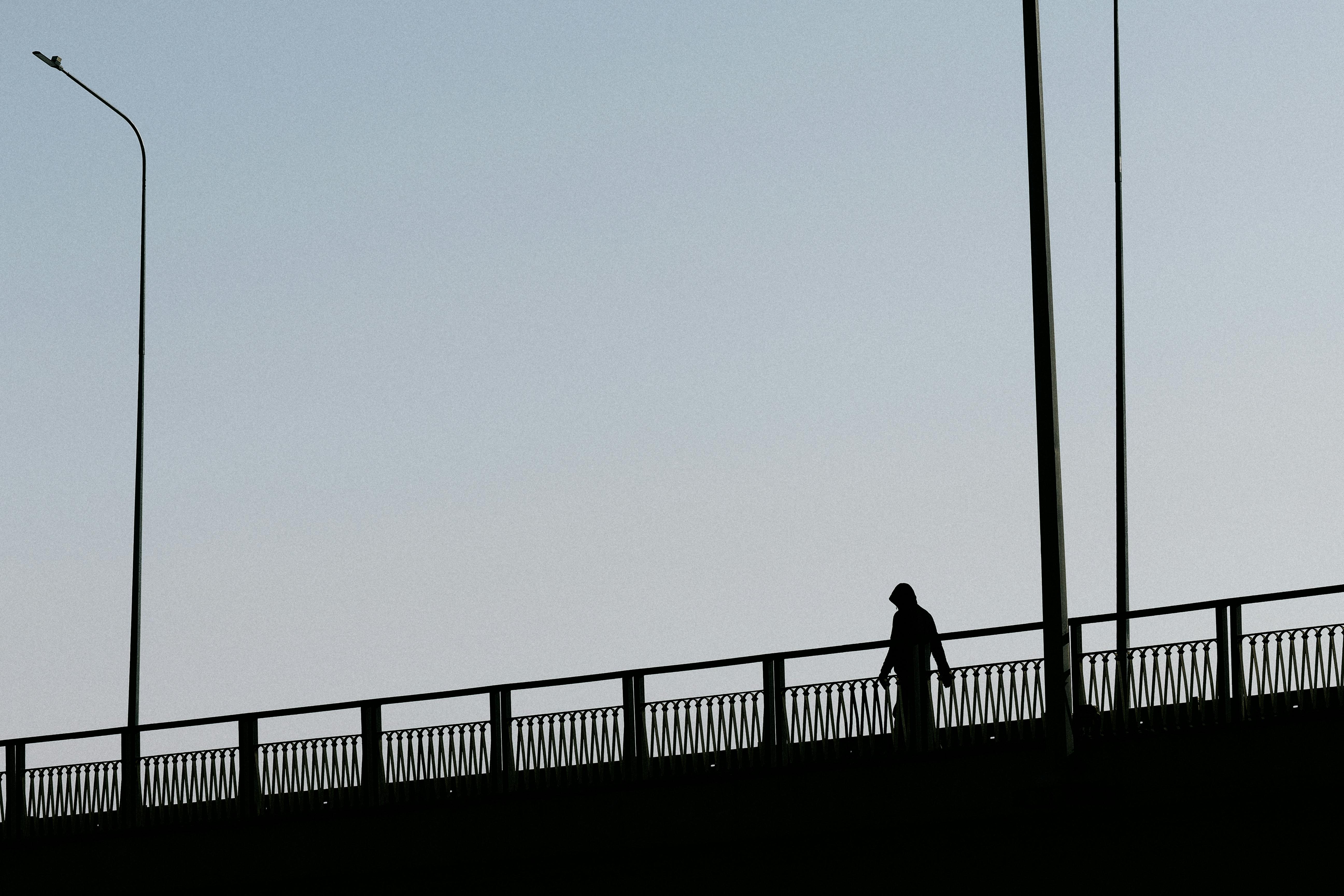ingyenes Egy személy sziluettje sétál egy hídon tiszta égbolt alatt alkonyatkor. Stockfotó