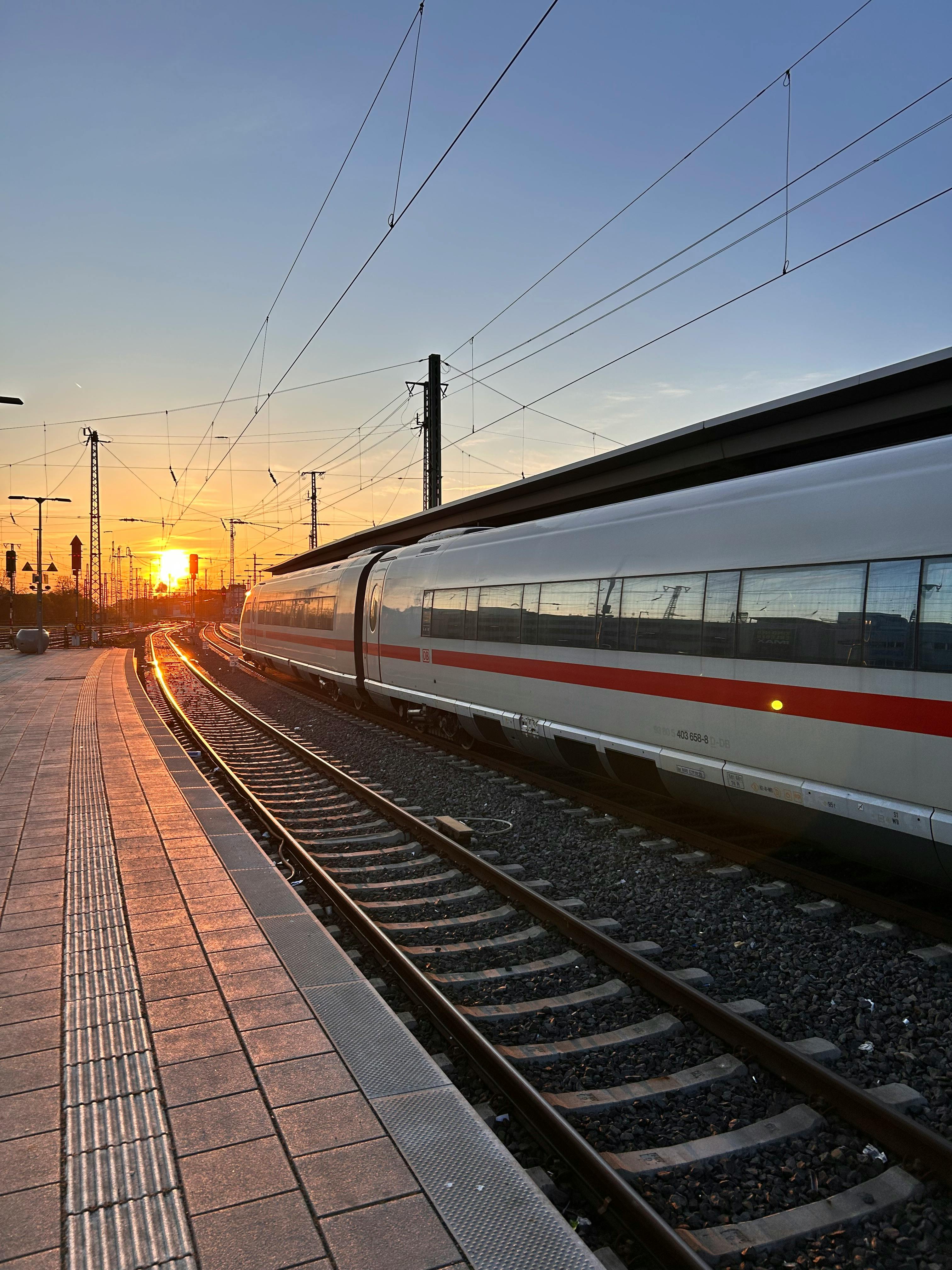 Gratis Et høyhastighetstog glir gjennom en jernbanestasjon ved solnedgang, og fremhever elegant moderne reiseliv. Arkivbilde