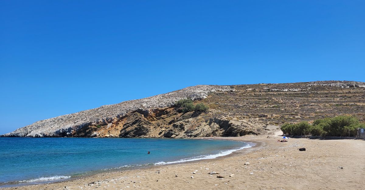 Idyllic beach view in Karavostasis, Folegandros, Greece with clear blue waters and rugged cliffs.
