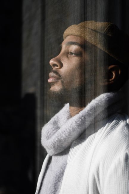A pensive man in stylish winter wear gazes thoughtfully out the window.