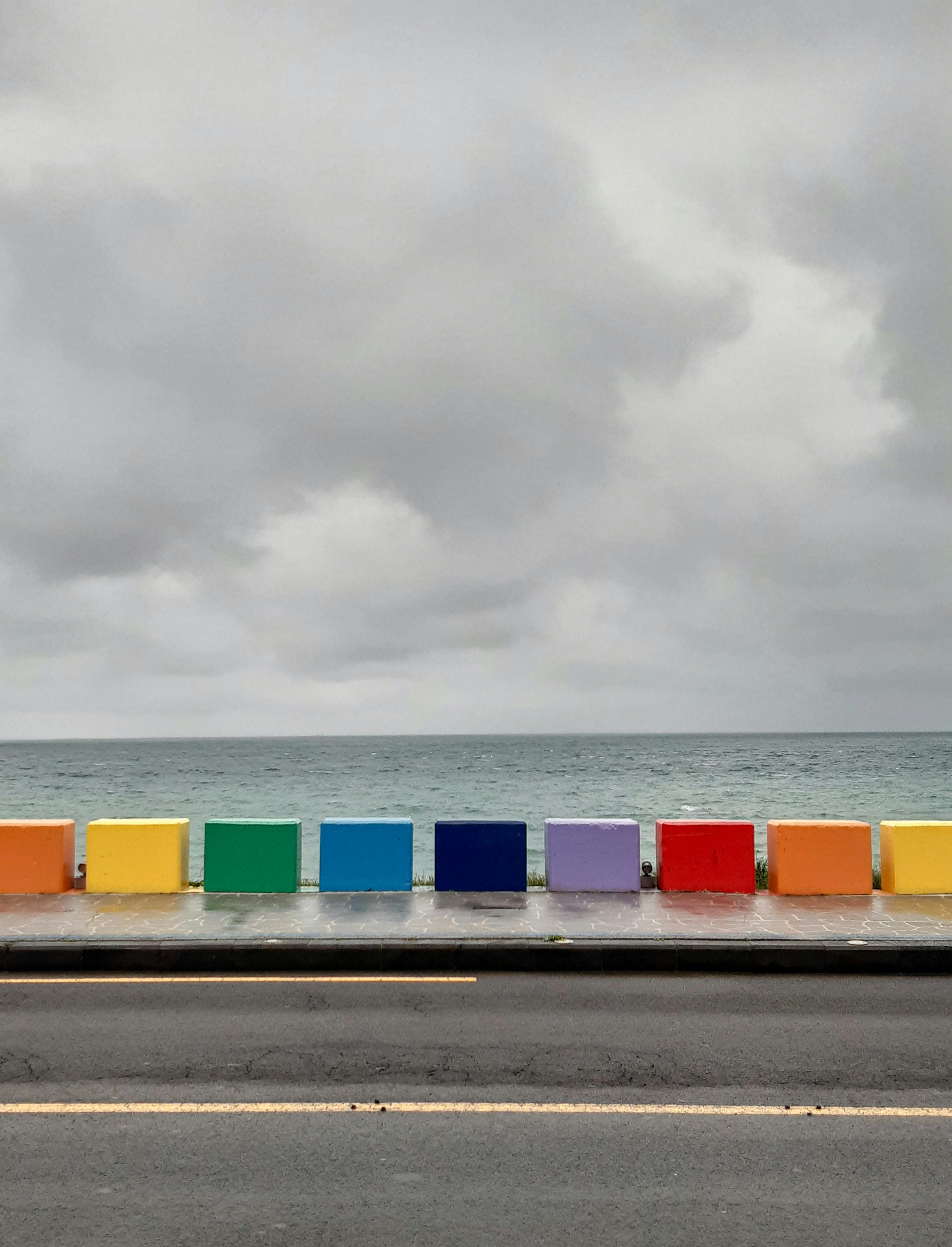 Kostenlos Leuchtend bunte Regenbogenbarrieren säumen eine Küstenstraße und bilden einen Kontrast zum ruhigen Ozean in Südkorea. Stock-Foto