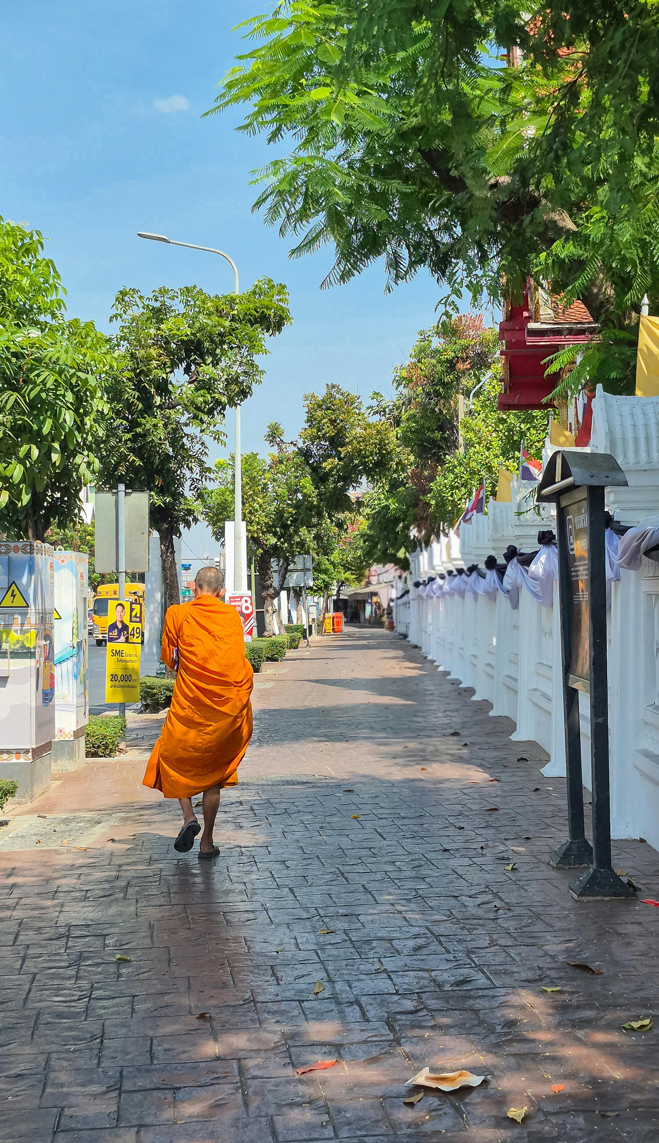 Gratuit Un moine bouddhiste en robe orange déambule dans une rue colorée de Bangkok, en Thaïlande. Photos