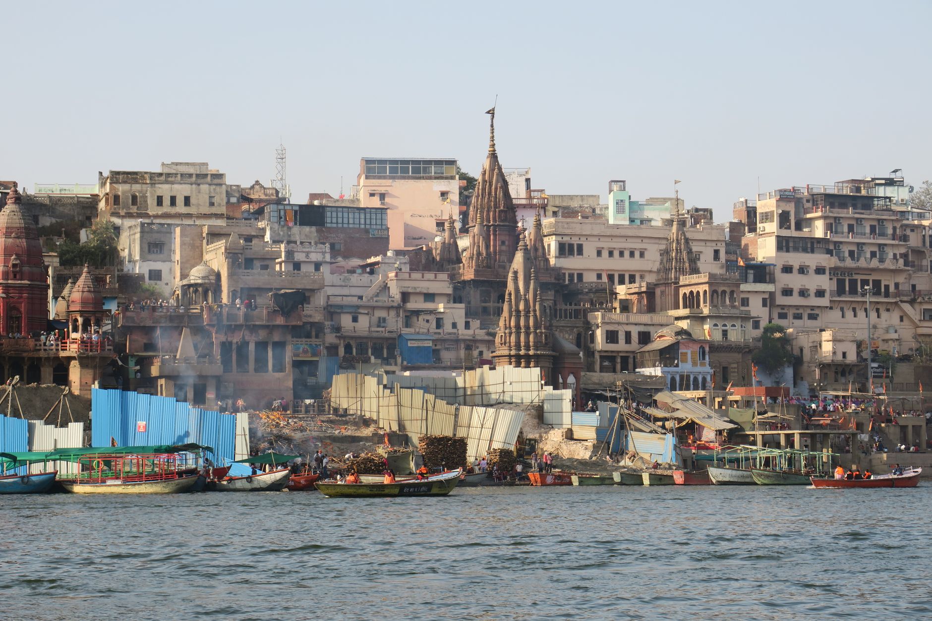 Lively scene of the ghats in Varanasi, India, with colorful boats and historic architecture along the Ganges River.