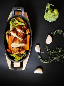 Top view of roasted chicken with vegetables in a pan on a dark background.