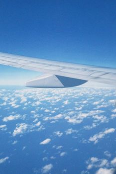 Scenic aerial view of airplane wing flying over clouds with a clear blue sky visible.