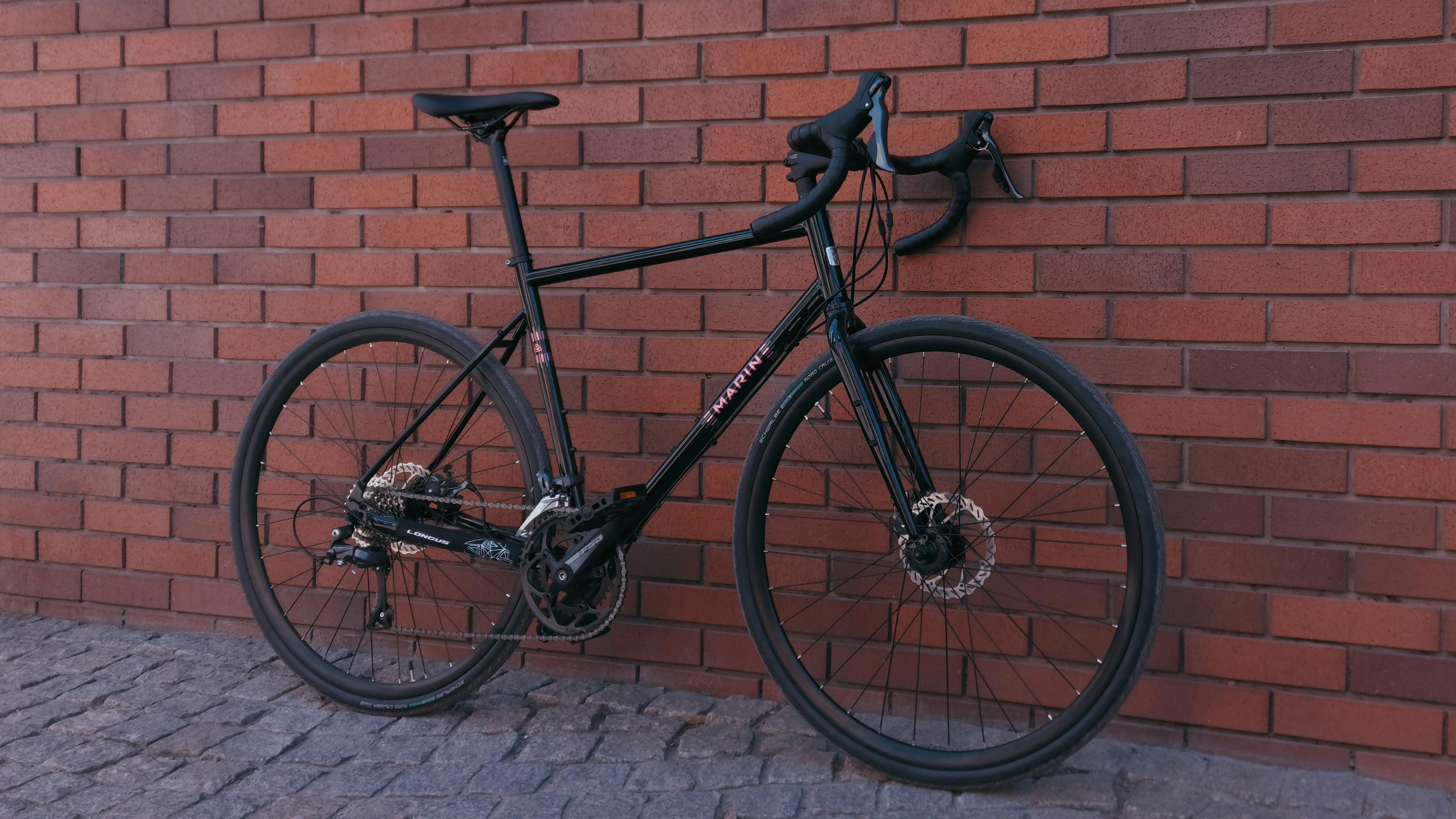 Gratis En elegant gravelcykel, Marin-modellen, hviler op ad en farverig murstensvæg og fremviser dens touring-egenskaber. Lagerfoto