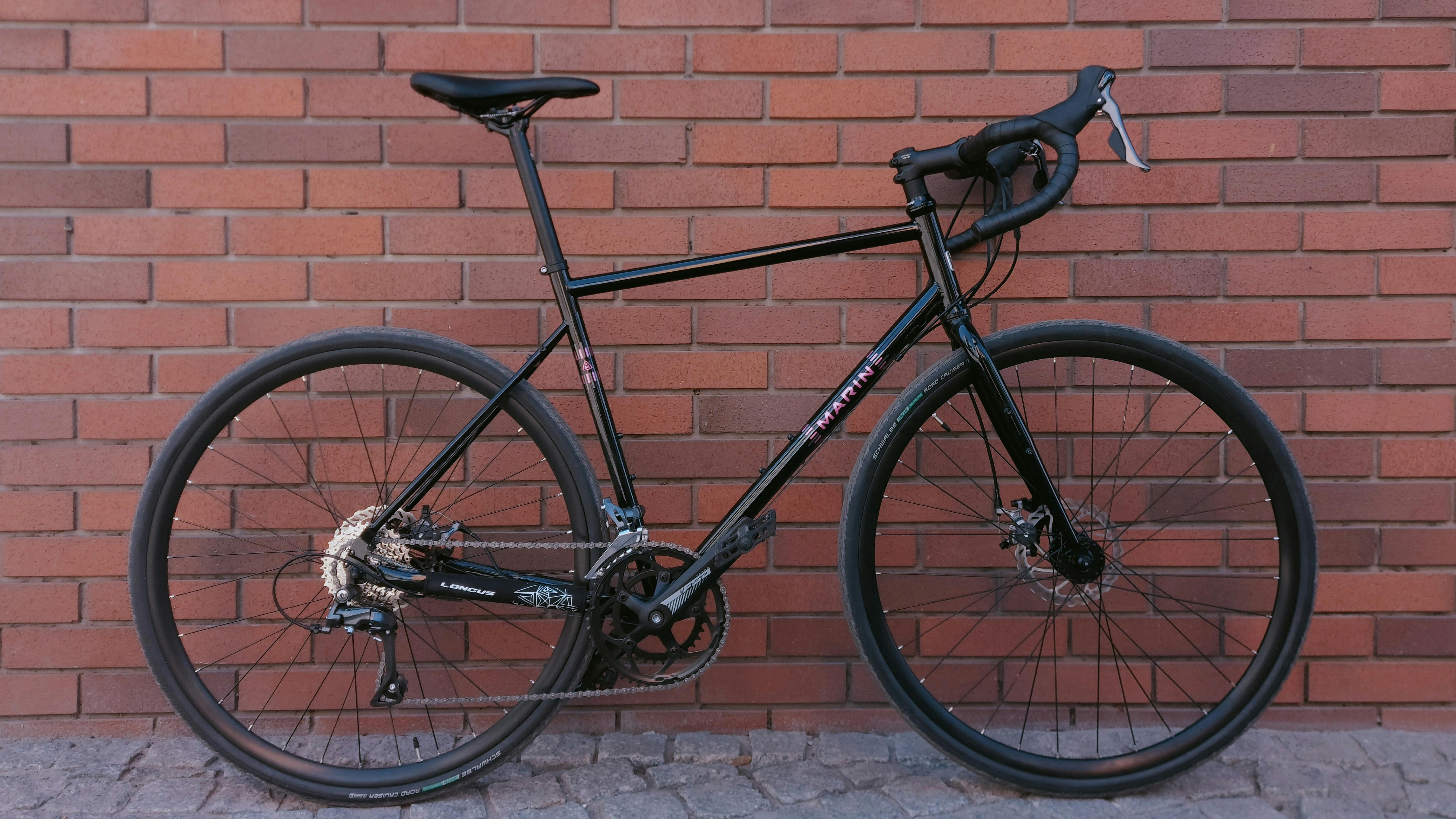 Gratis Elegant sort gravelcykel parkeret op ad en rustik rød murstensvæg, perfekt til by- eller cykelture. Lagerfoto