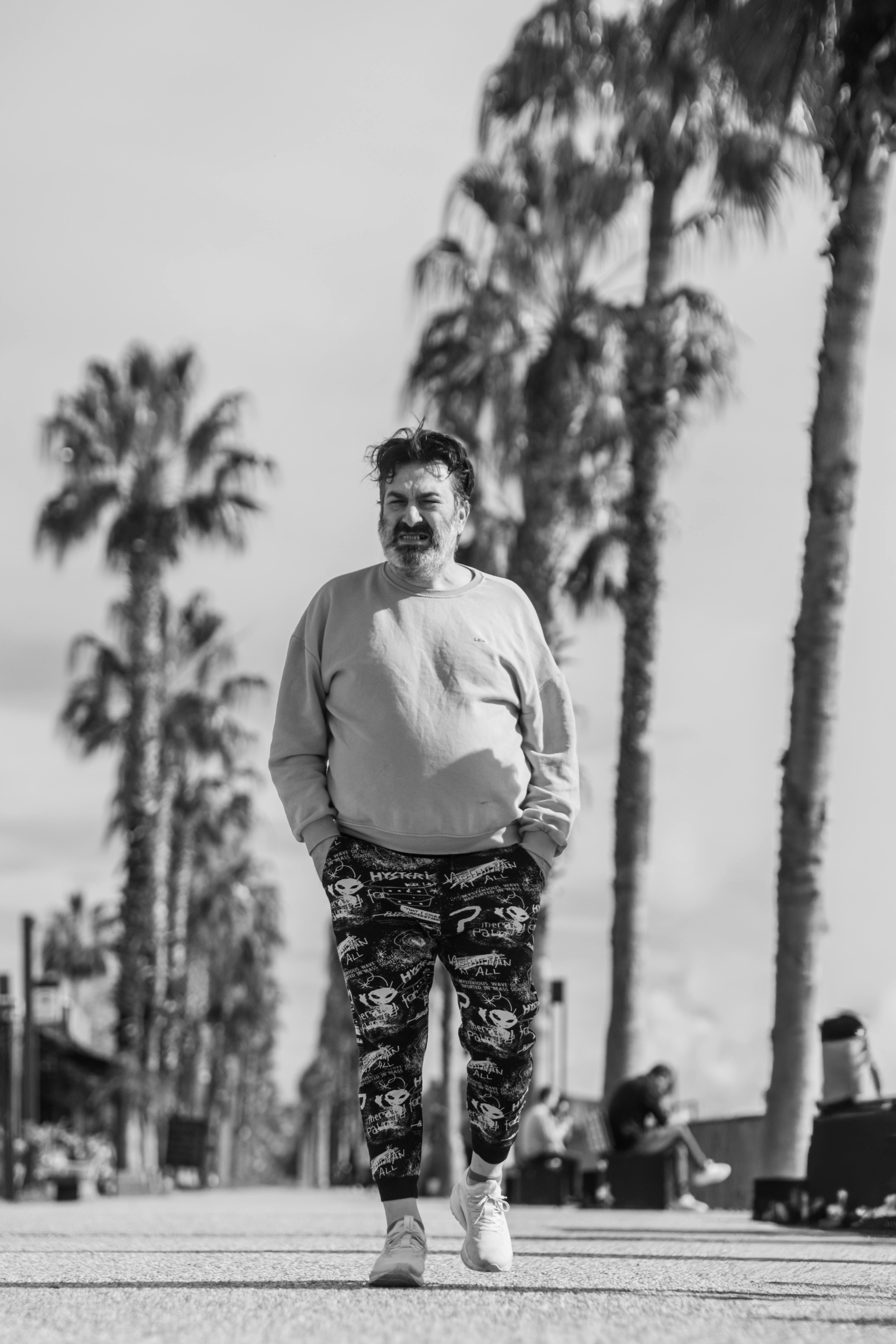 Free Adult man walking on a palm tree-lined street on a sunny day. Stock Photo