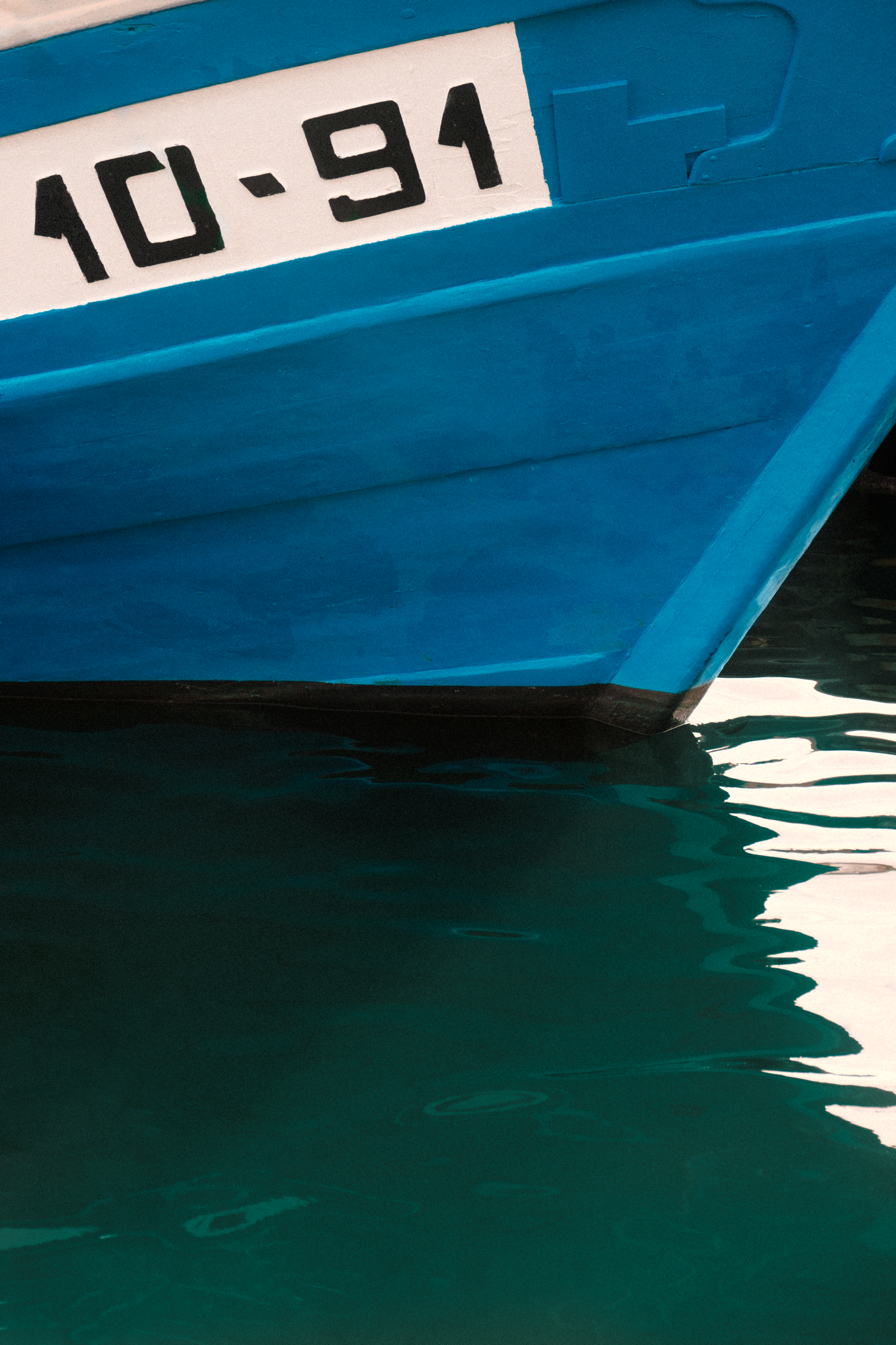 Close-up of a blue boat hull with water reflection, docked in Tarragona harbor.