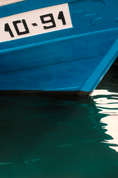 Close-up of a blue boat hull with water reflection, docked in Tarragona harbor.