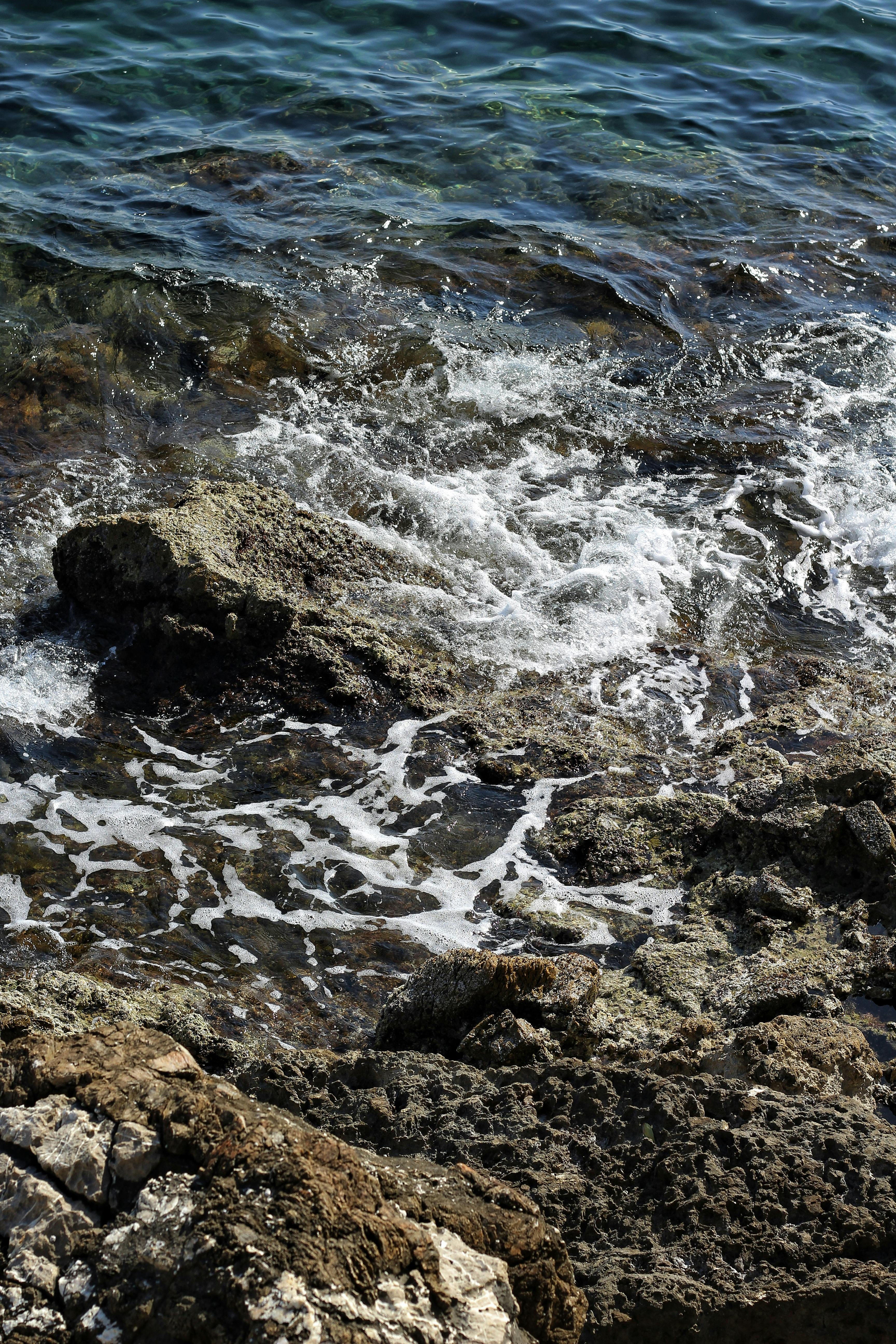Ücretsiz Kayalık kıyı şeridine çarpan dalgaların büyüleyici manzarası, doğanın ham gücünü ve güzelliğini sergiliyor. Stok Fotoğraflar