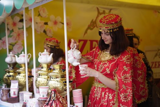 Young woman in traditional attire serving tea at a vibrant cultural festival. Captivating scene.